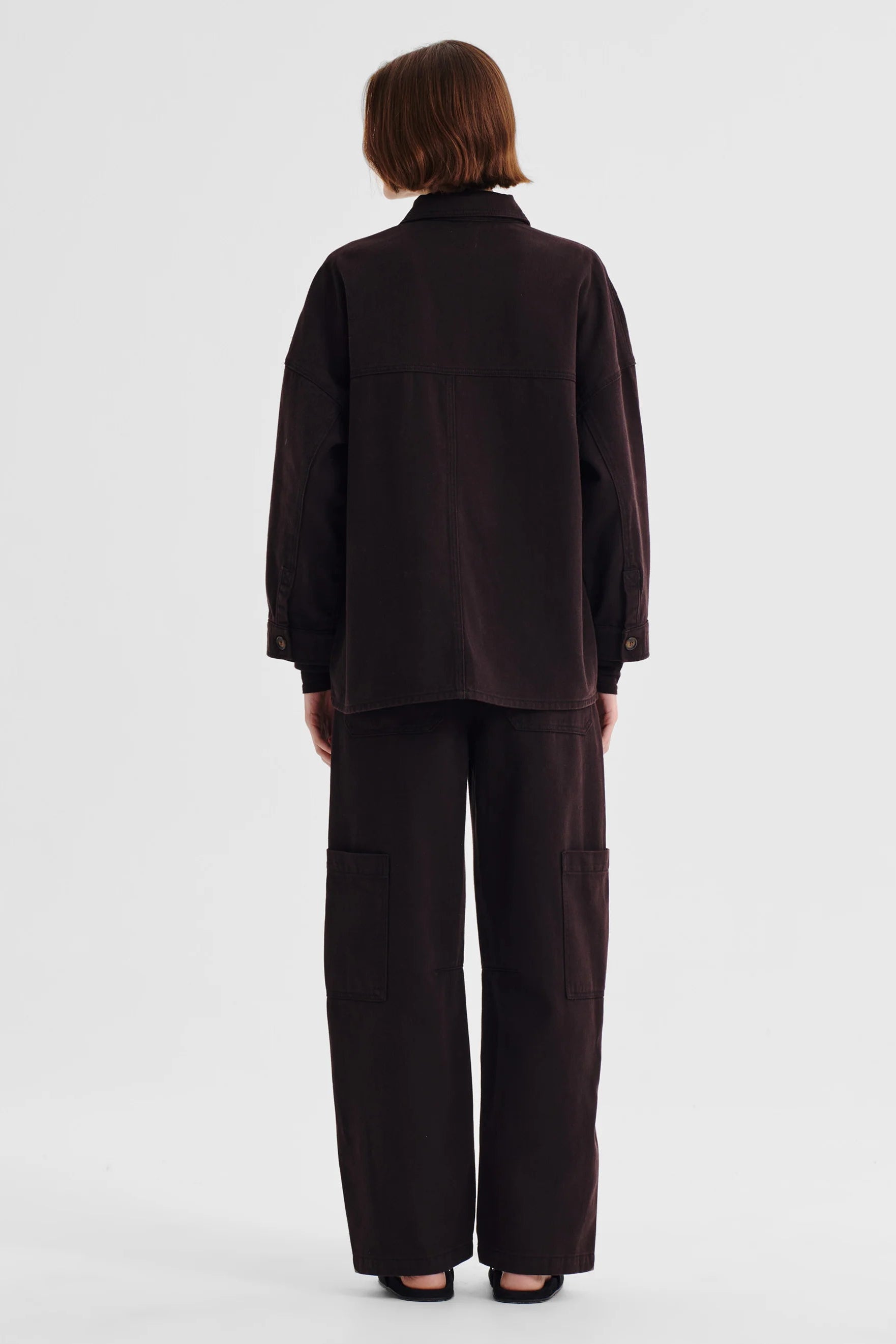 Women wearing dark brown denim shirt jacket and matching denim pant on a white background. 