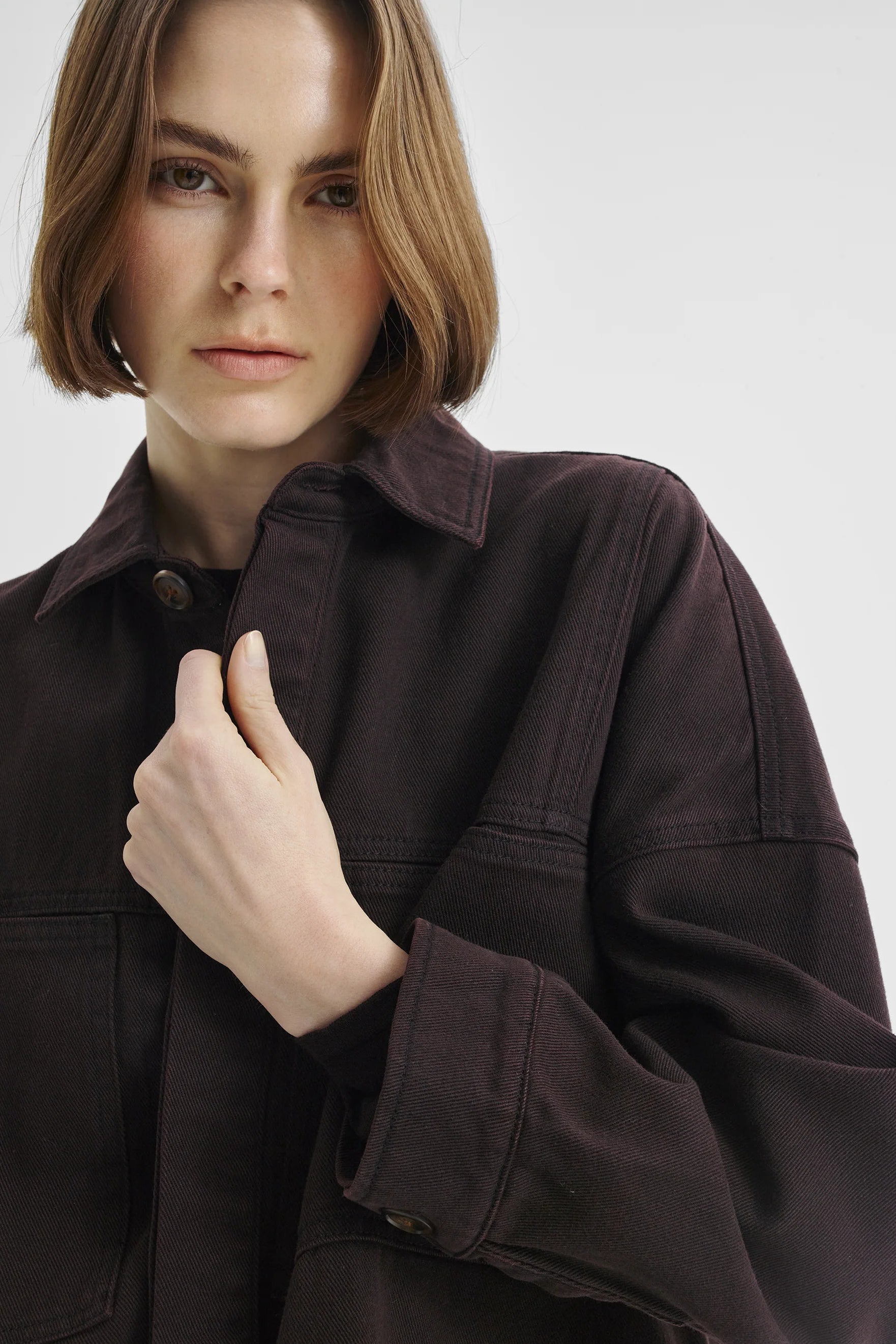 Women wearing dark brown denim shirt jacket on a white background. 
