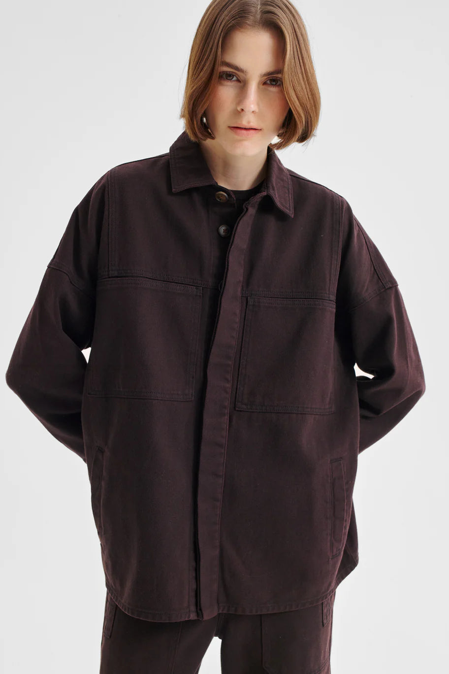 Women wearing dark brown denim shirt jacket and matching denim pant on a white background. 