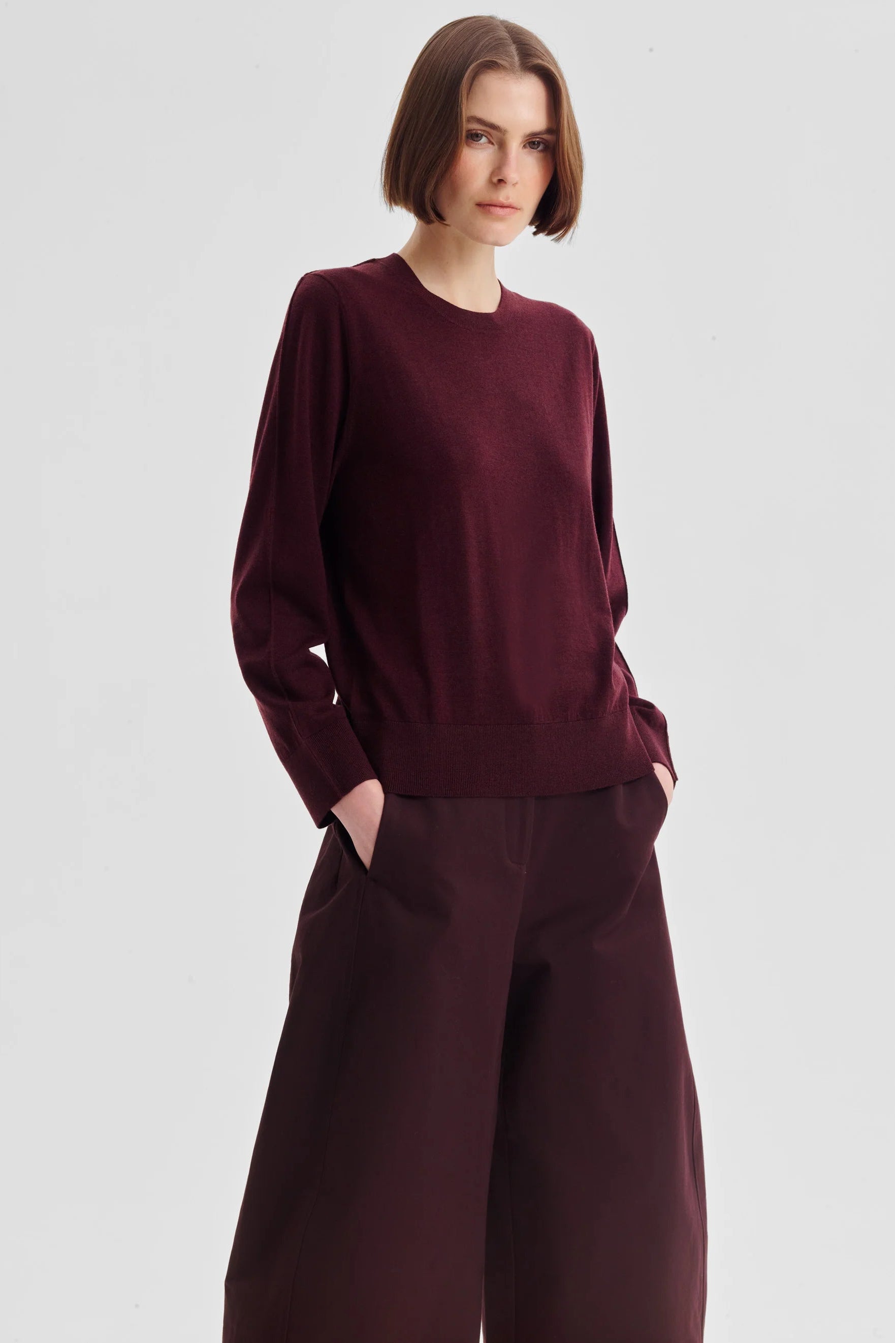 Women wearing a pinot red colour merino knit top and matching pant wth sandals on a white background. 