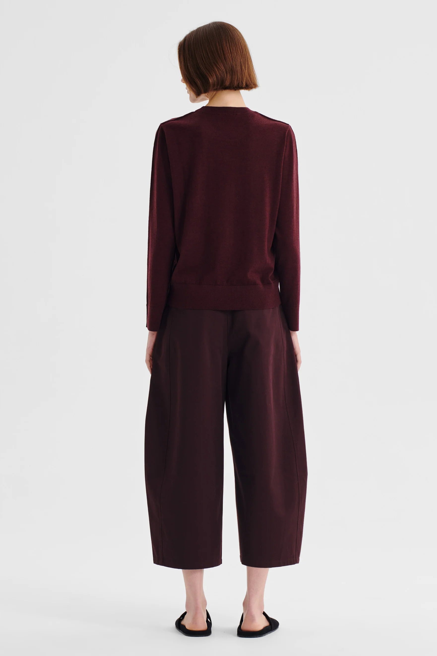 Women wearing a pinot red colour merino knit top and matching pant wth sandals on a white background. 