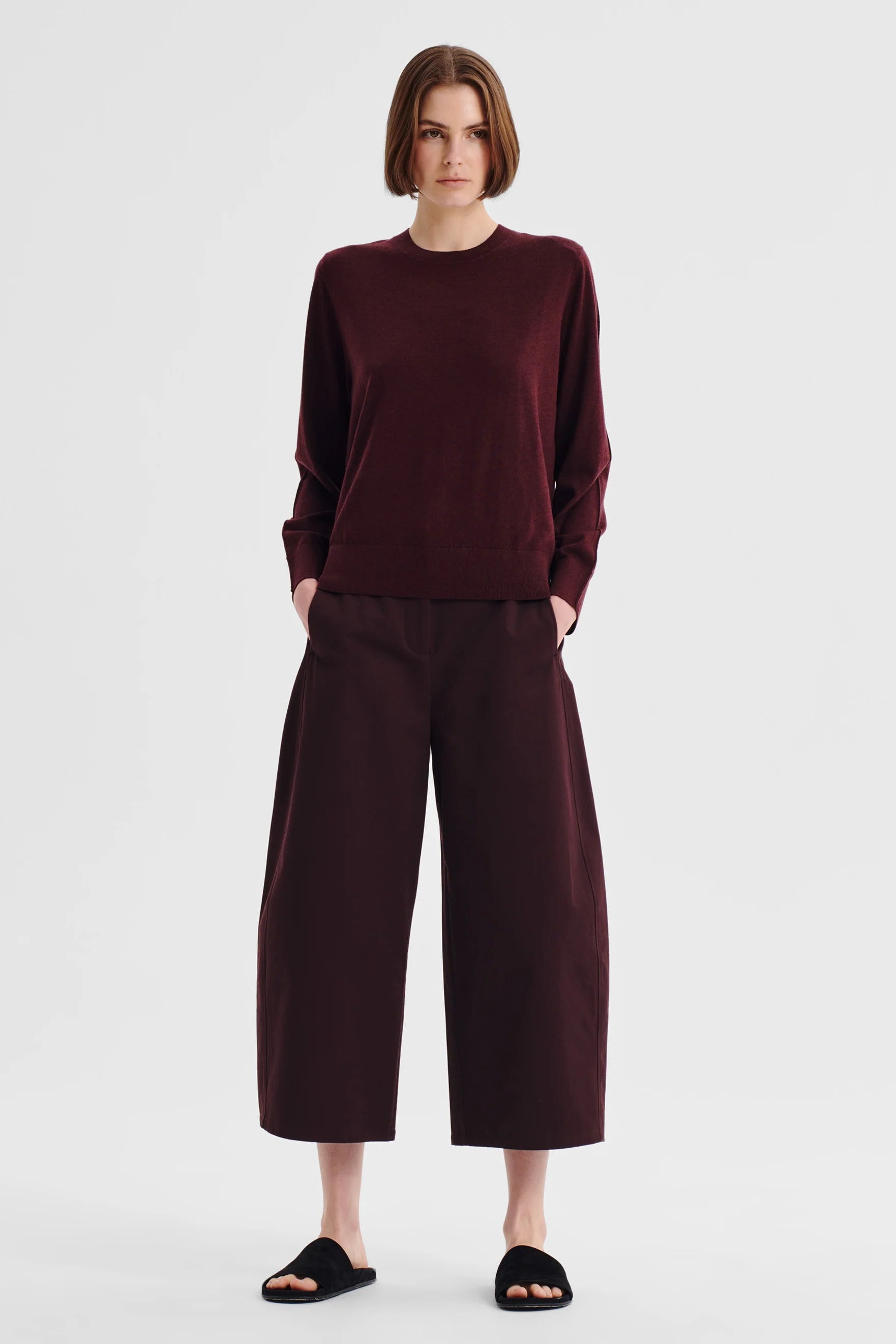 Women wearing a pinot red colour merino knit top and matching pant wth sandals on a white background. 