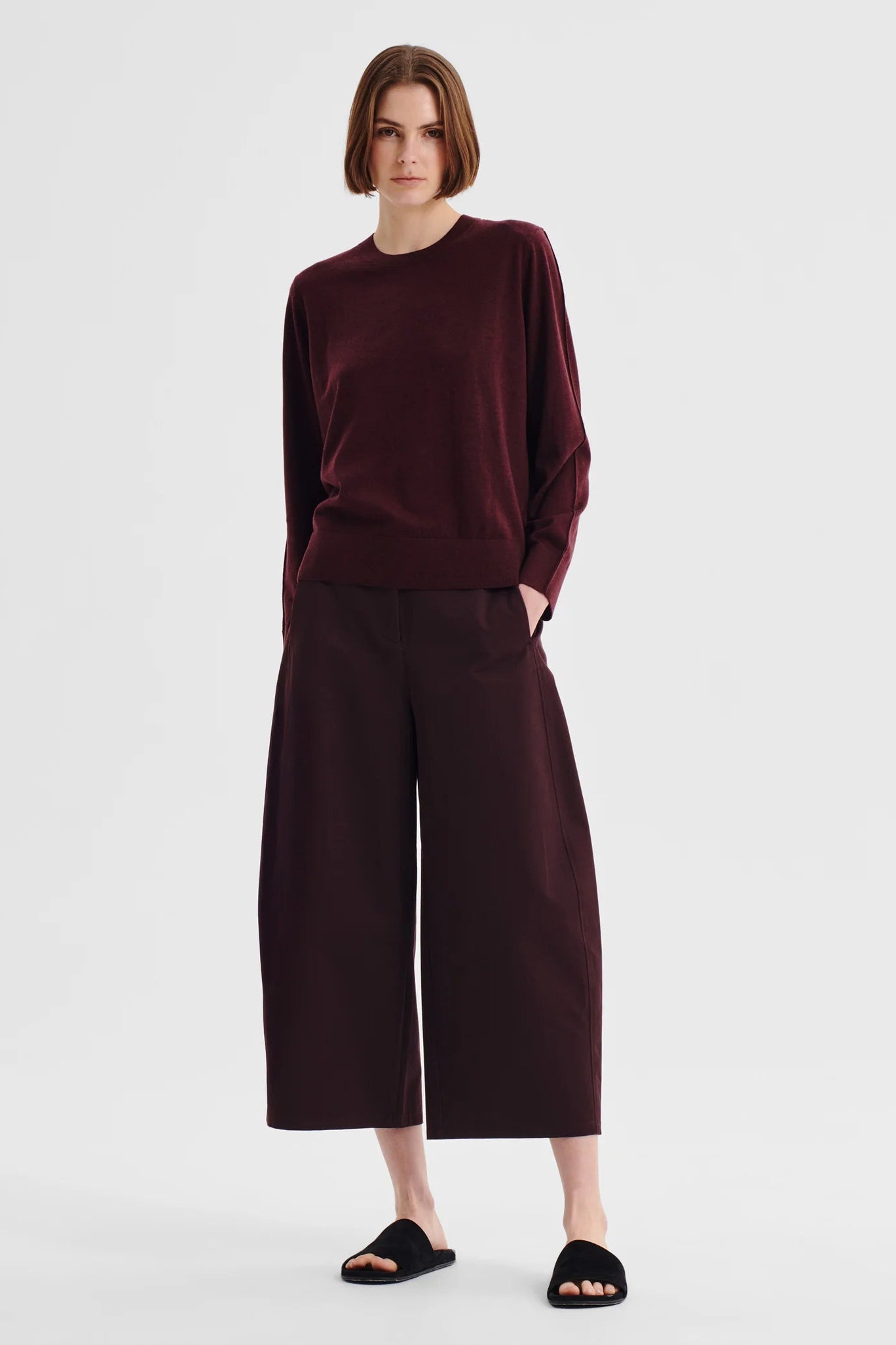 Women wearing a pinot red colour merino knit top and matching pant wth sandals on a white background. 