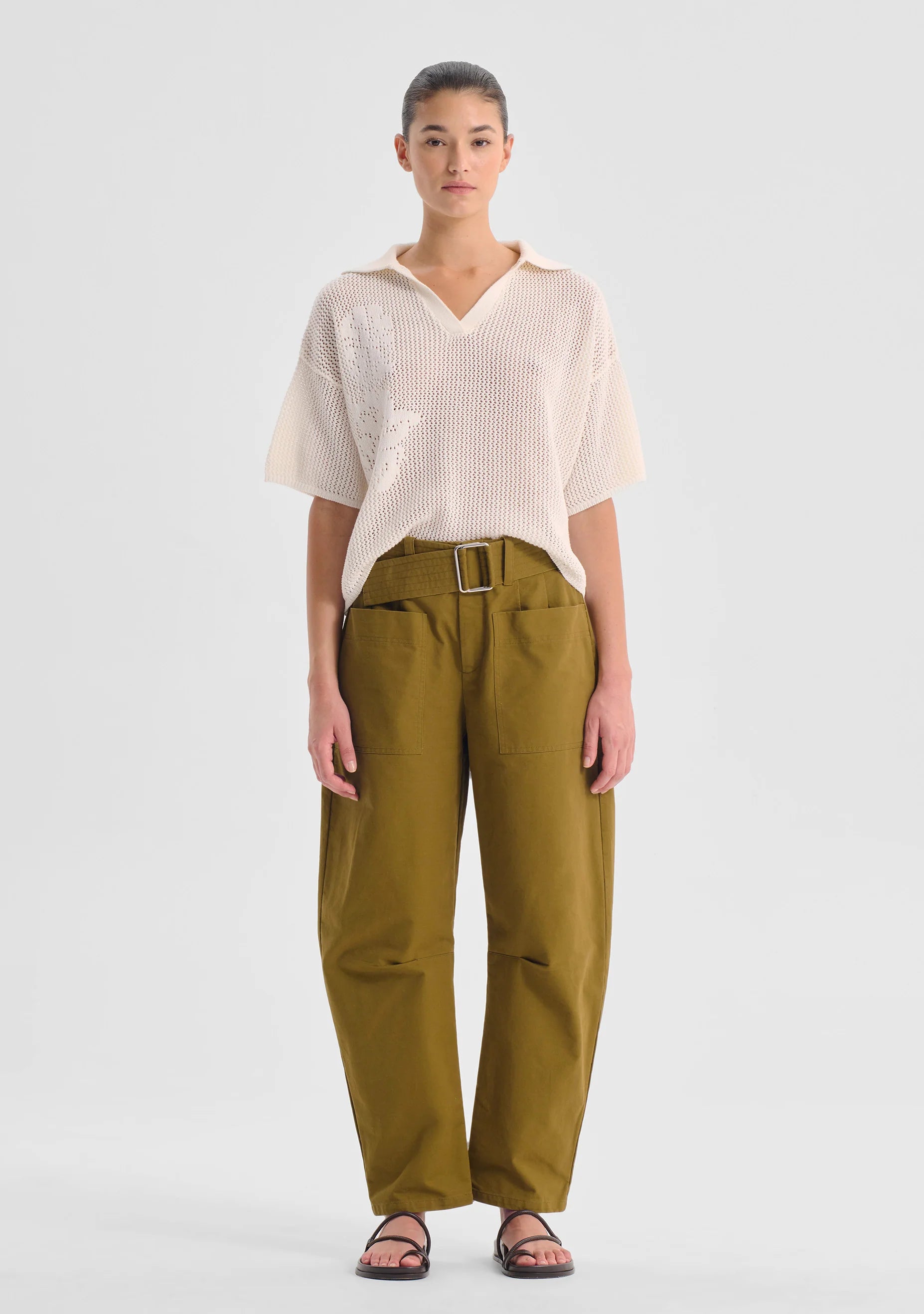 Woman wearing a white top and green pants on a light gray background