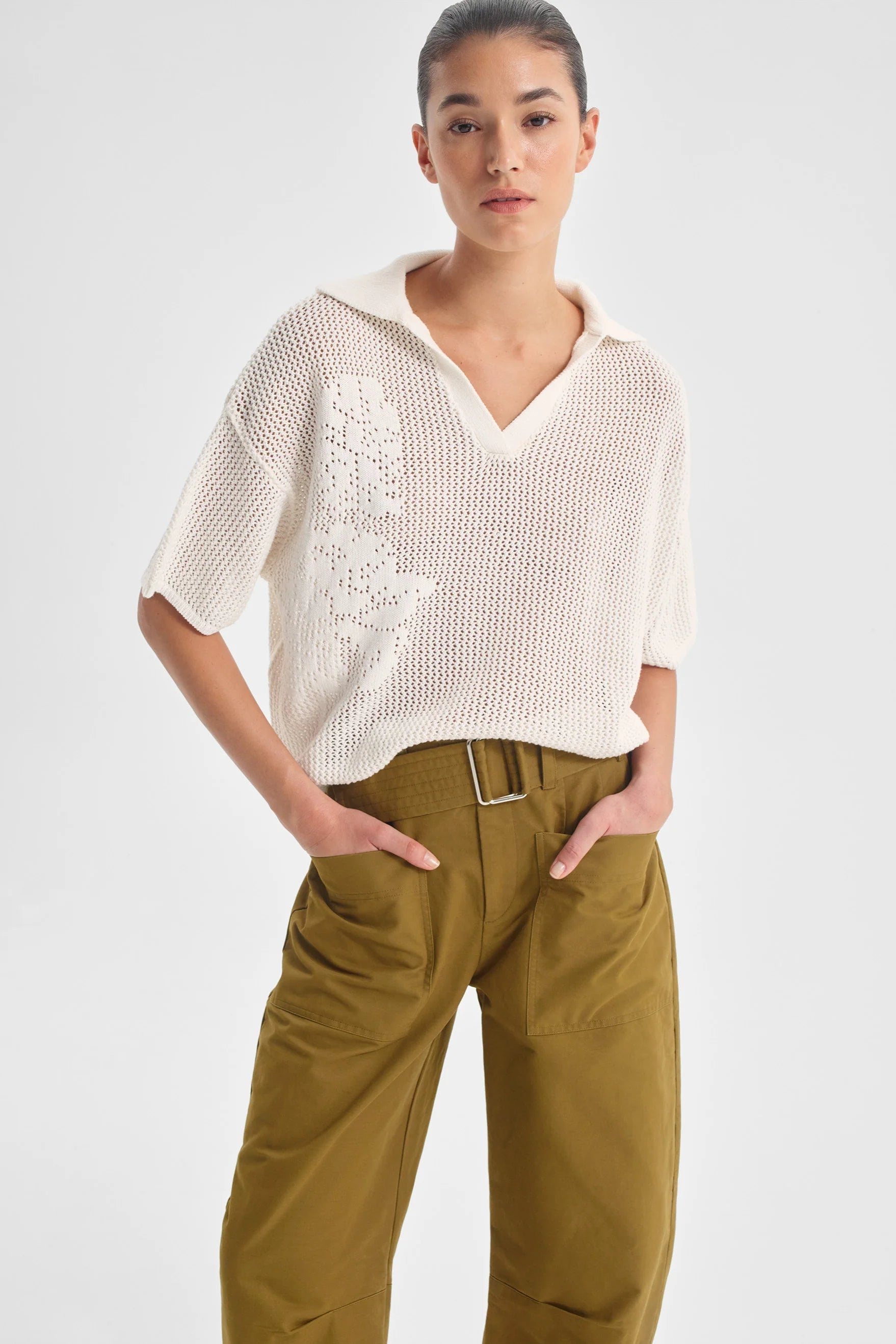 Person wearing a white knit top and green pants on a light gray background