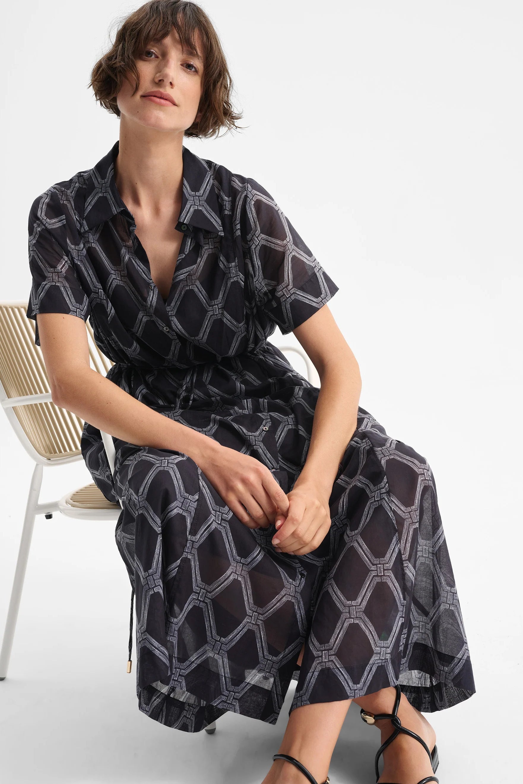 Woman wearing a black and white patterned dress sitting on a chair against a white background