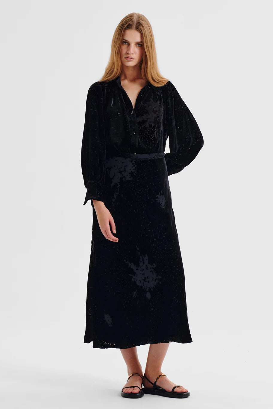 Woman wearing a black Velvet shirt with beaded button detailing and billow sleeves and matching skirt  on a white background. 