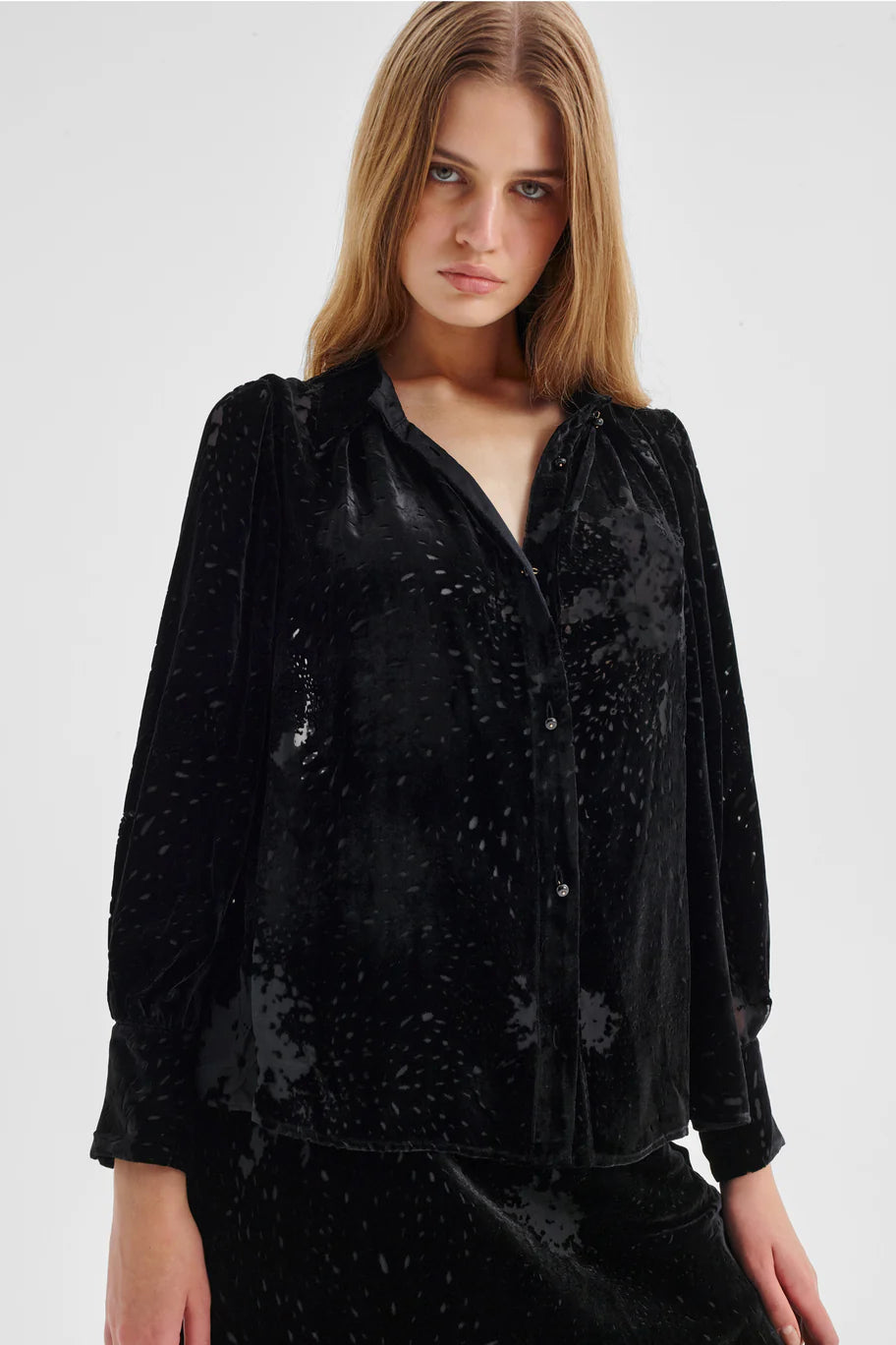 Woman wearing a black Velvet shirt with beaded button detailing and billow sleeves on a white background. 