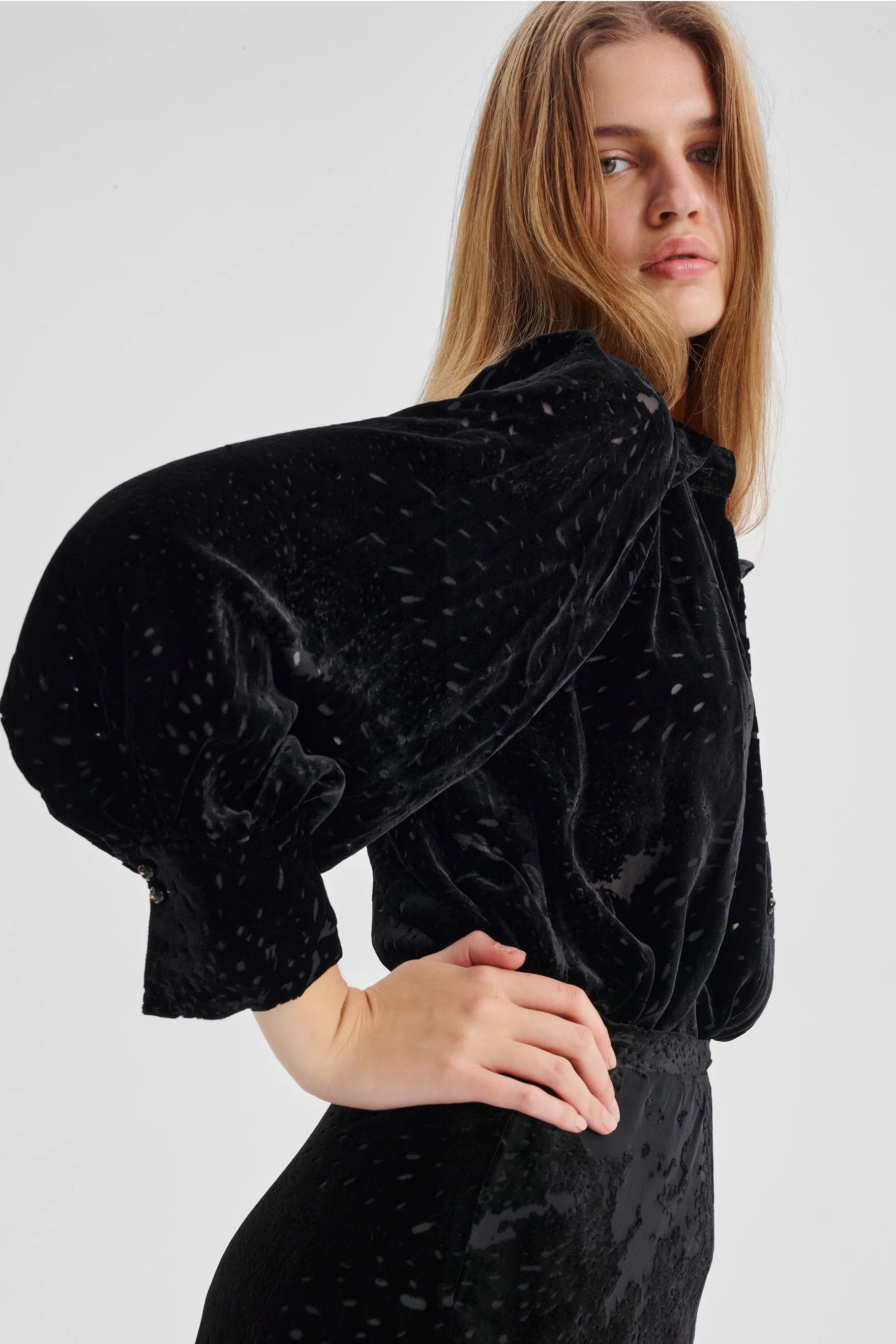 Woman wearing a black velvet outfit with puffed sleeves on a white background