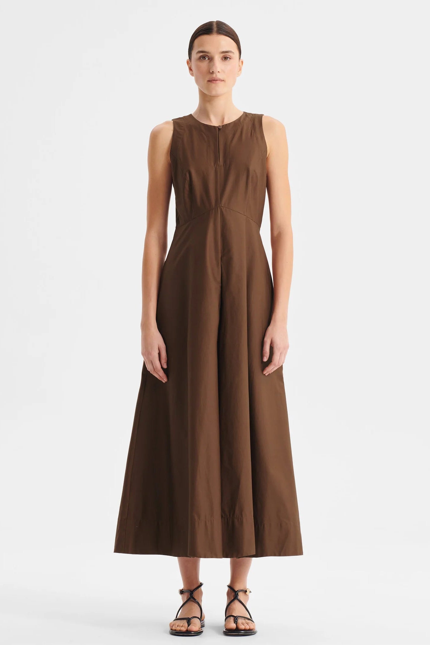 Model wearing sleeveless chocolate brown midi length dress with fitted bodice and full skirt on a white background. 