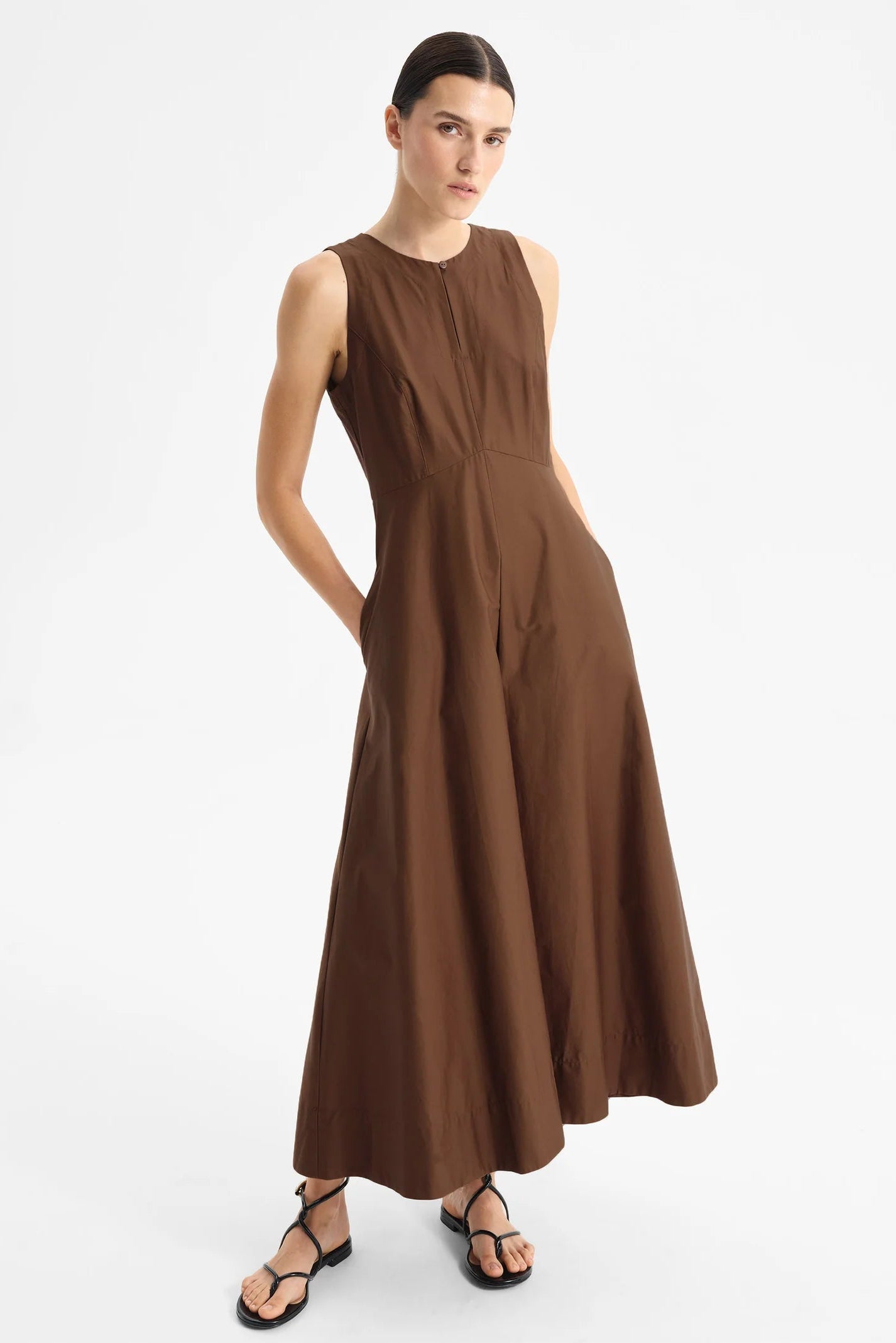 Model wearing sleeveless chocolate brown midi length dress with fitted bodice and full skirt on a white background. 