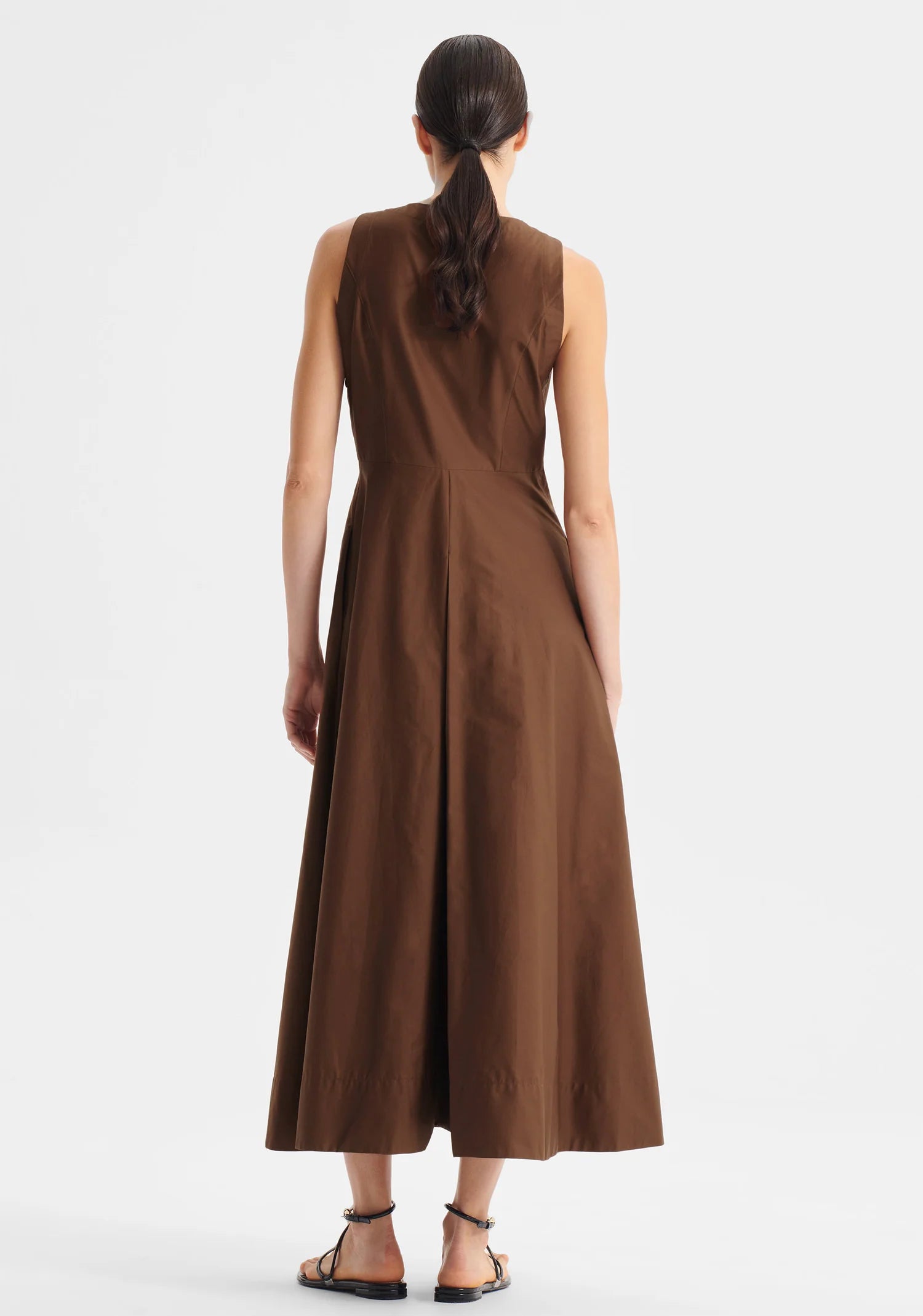 Model wearing sleeveless chocolate brown midi length dress with fitted bodice and full skirt. view of the back of the dress on a white background.  