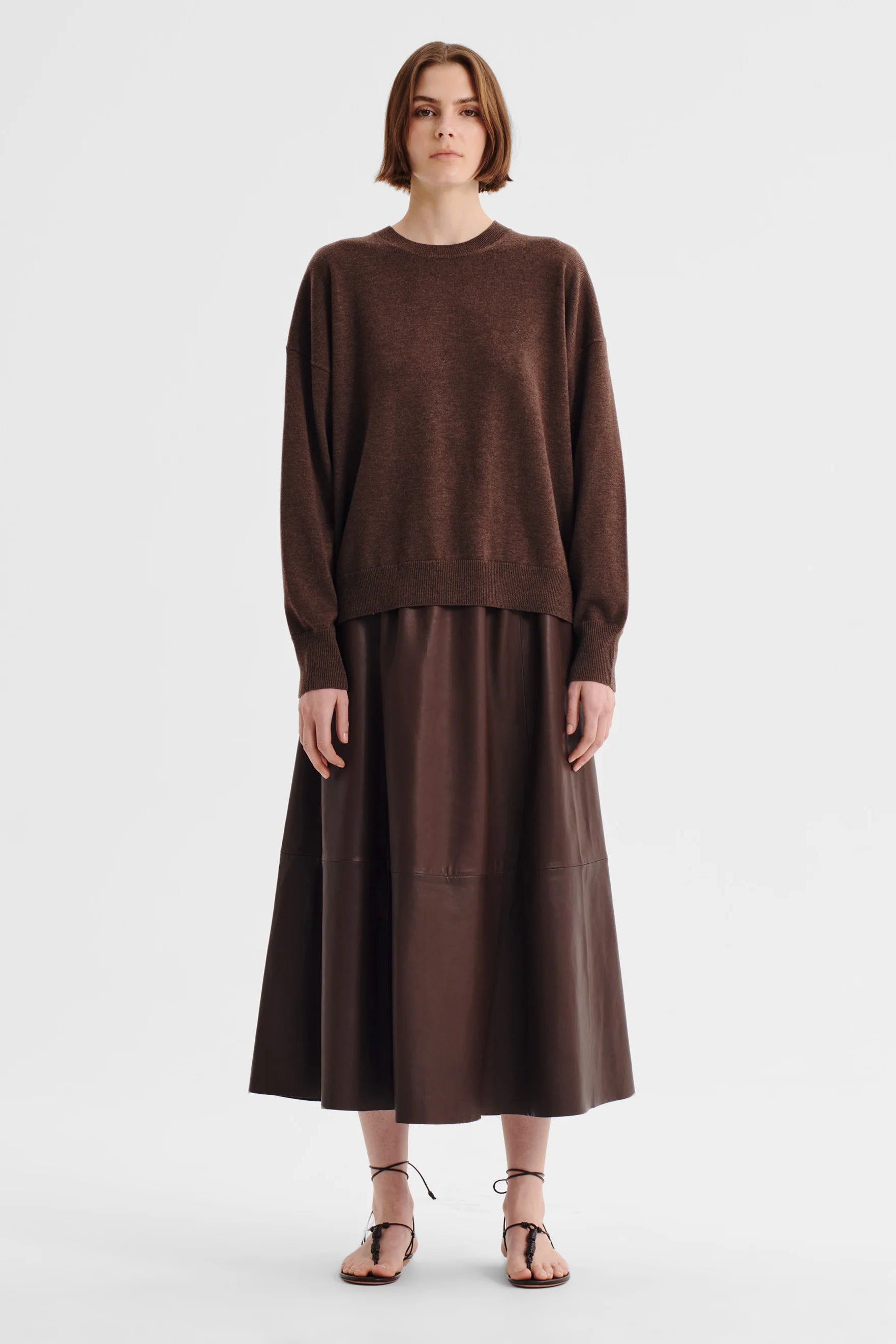 Women wearing a chocolate brown crew neck sweater and brown skirt on a white background. 