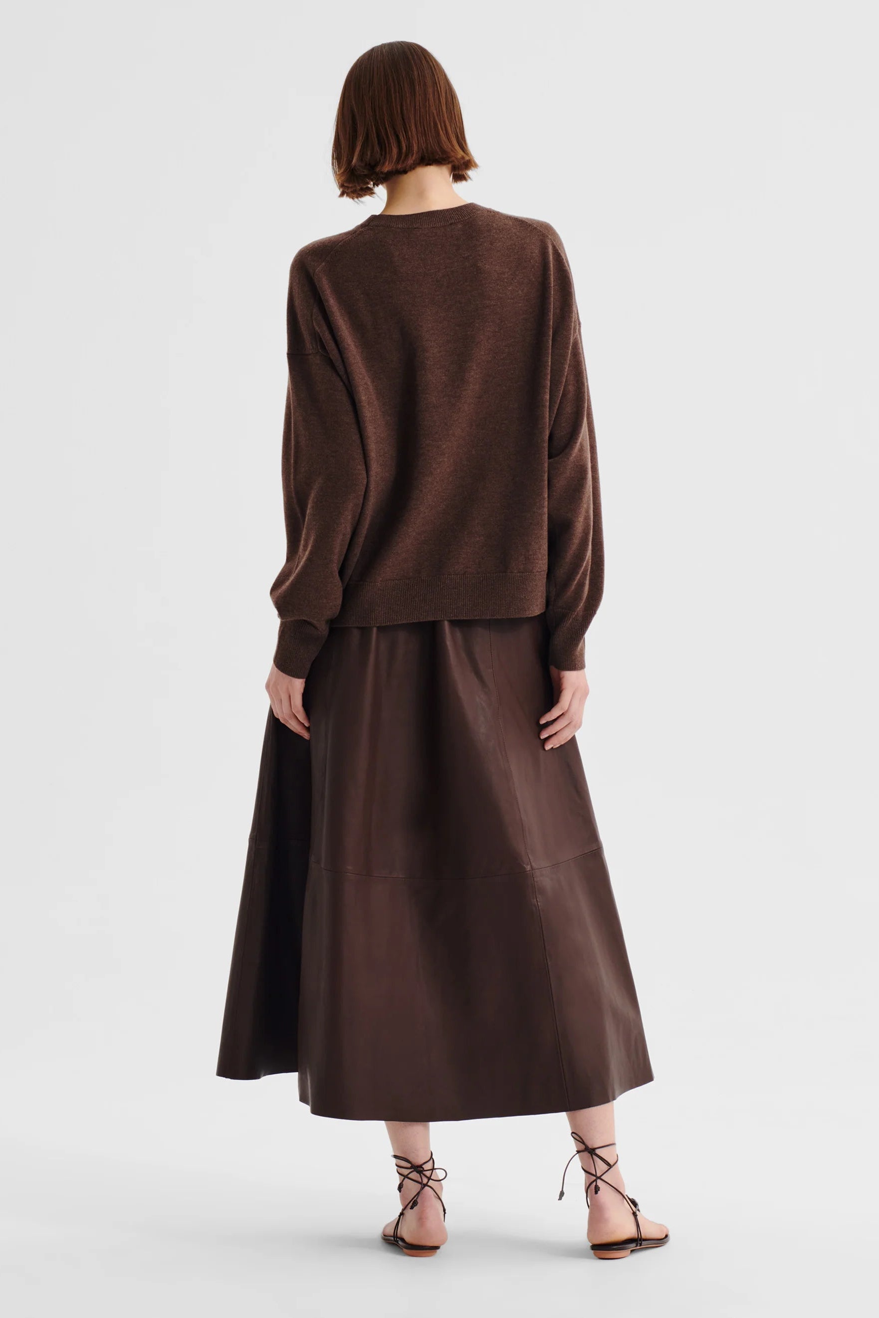 Women wearing a chocolate brown crew neck sweater and brown skirt on a white background. 
