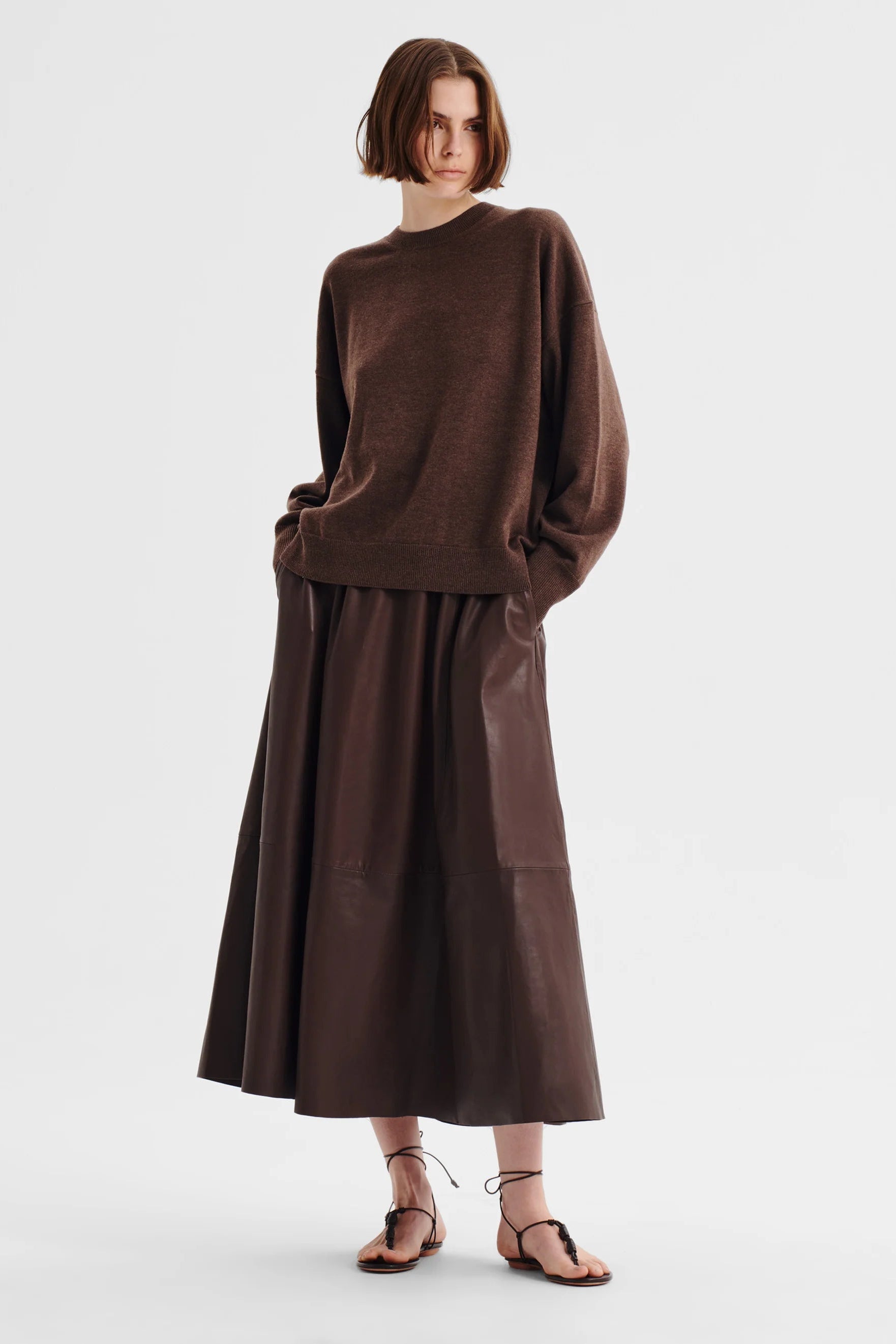 Women wearing a chocolate brown crew neck sweater and brown skirt on a white background. 