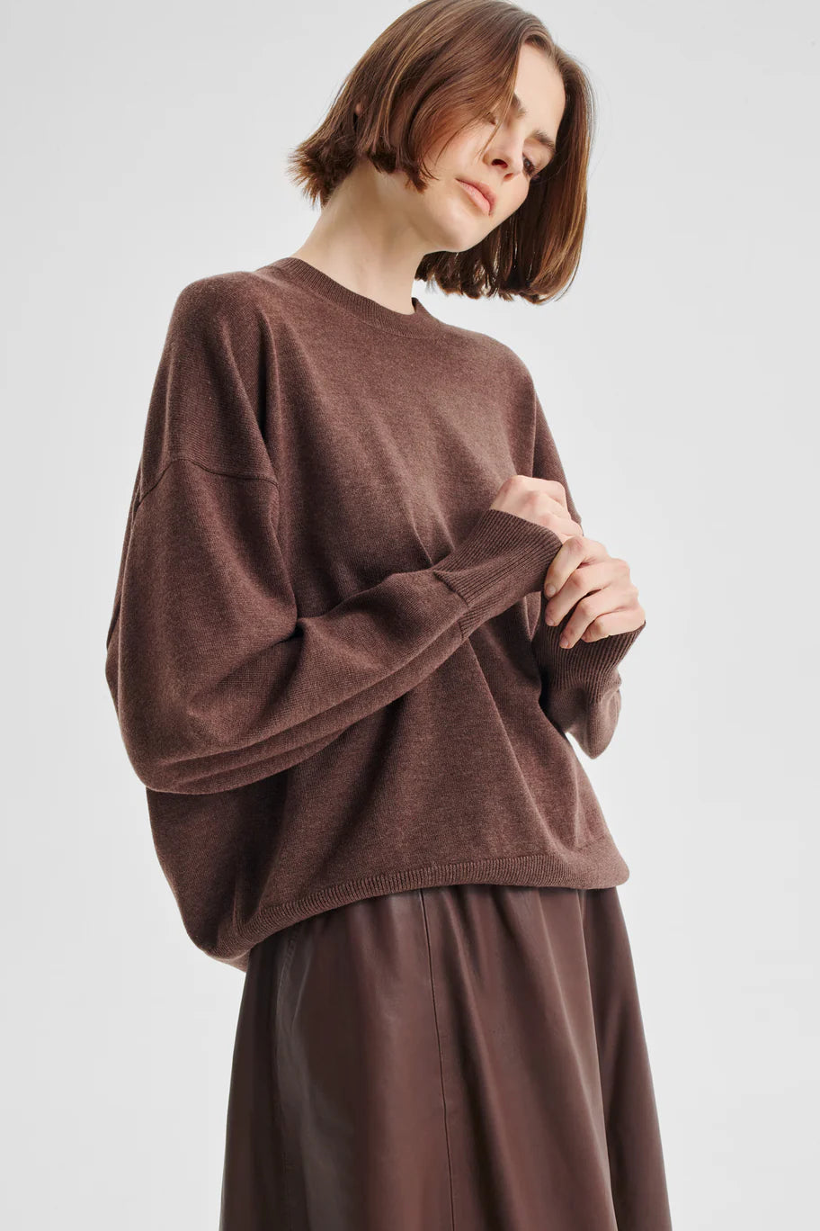 Women wearing a chocolate brown crew neck sweater and brown skirt on a white background. 