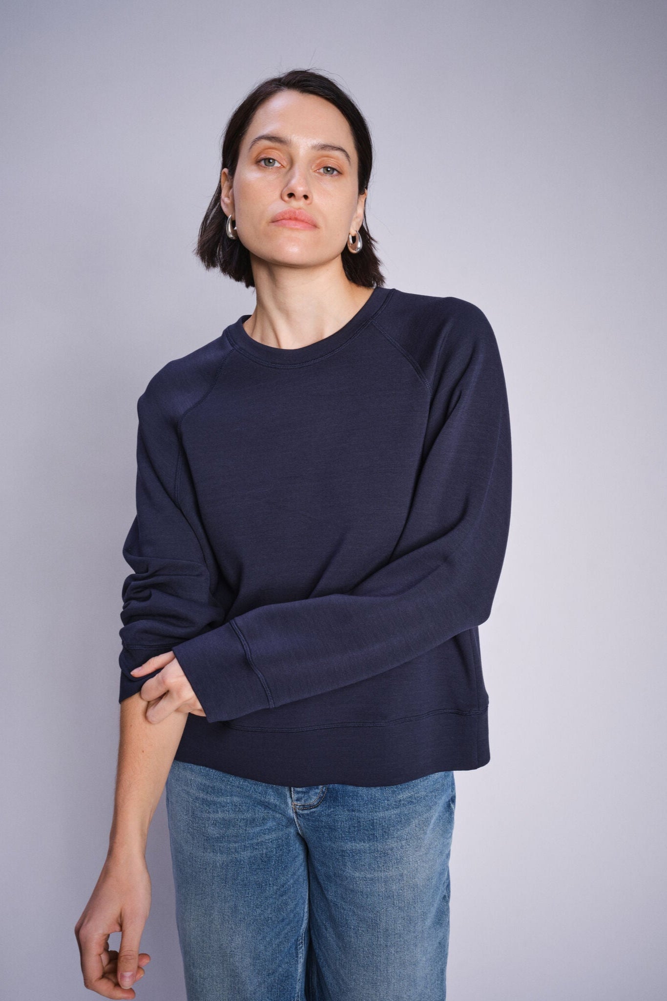 Model wearing a navy blue crew neck sweatshirt paired with denim jeans on a white background