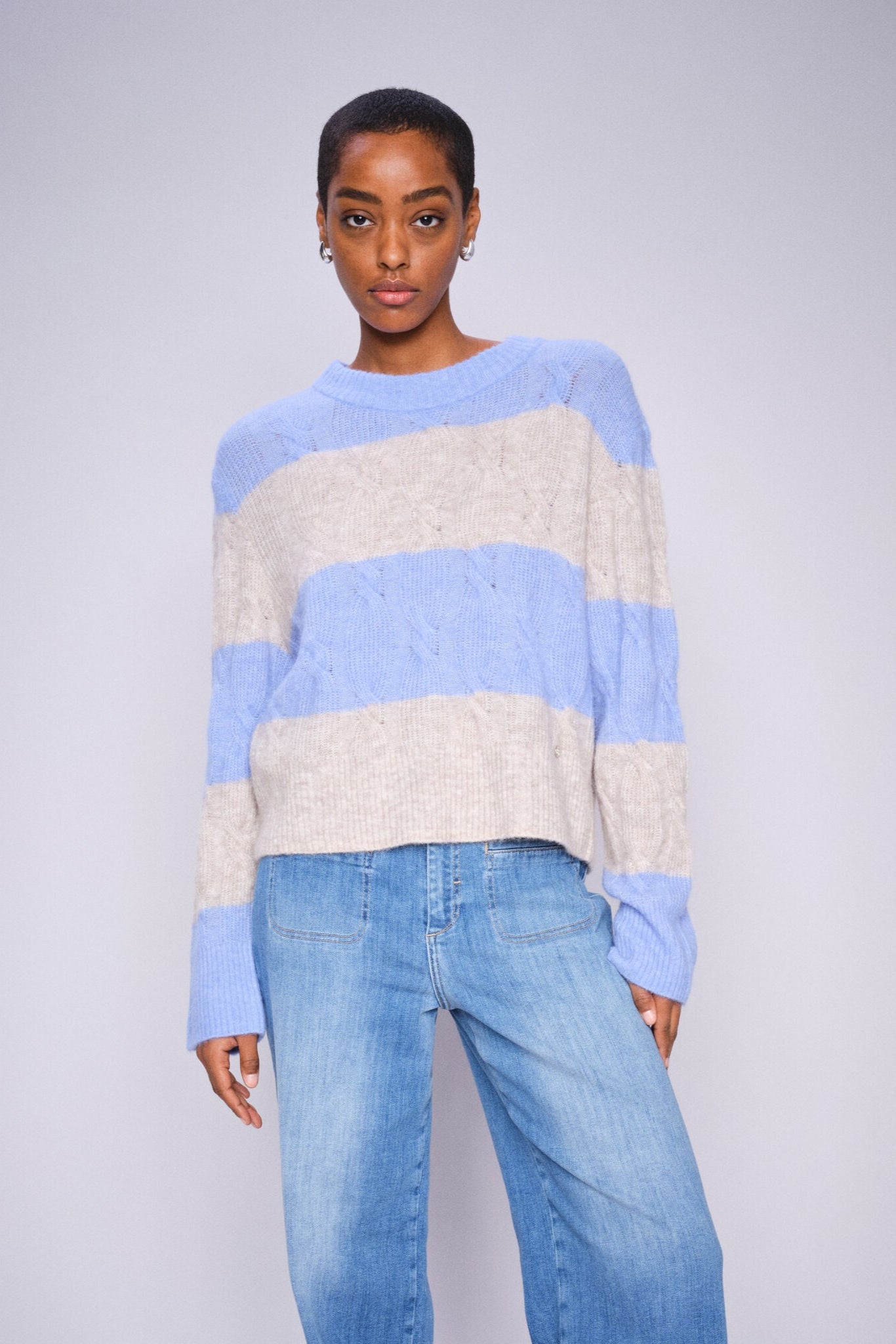 Person wearing a blue and white striped sweater with jeans on a plain background