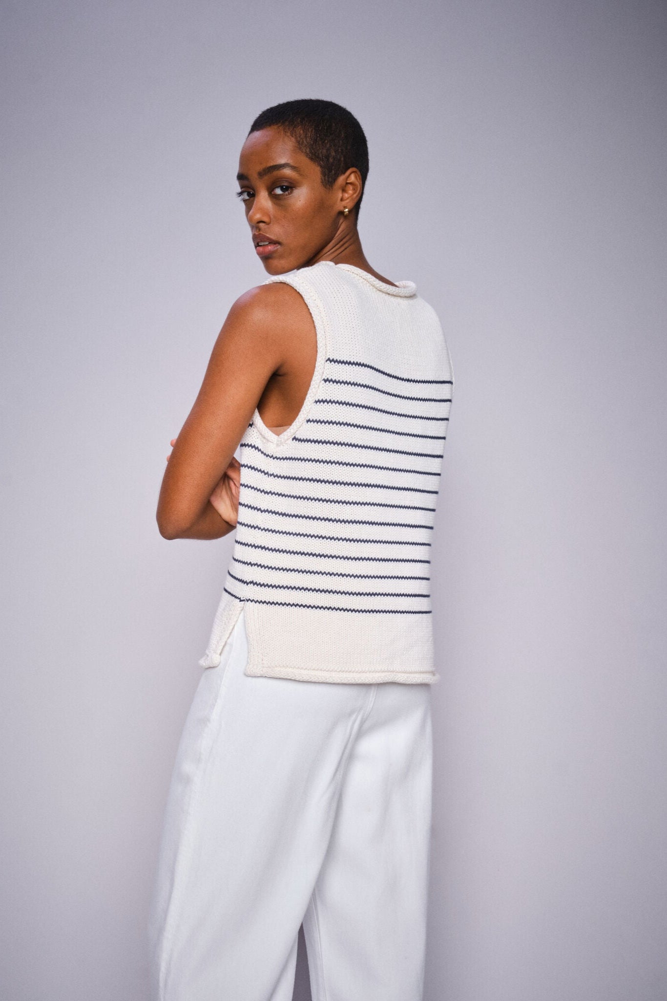 Woman wearing a white and black striped sleeveless top with light gray pants on a plain background