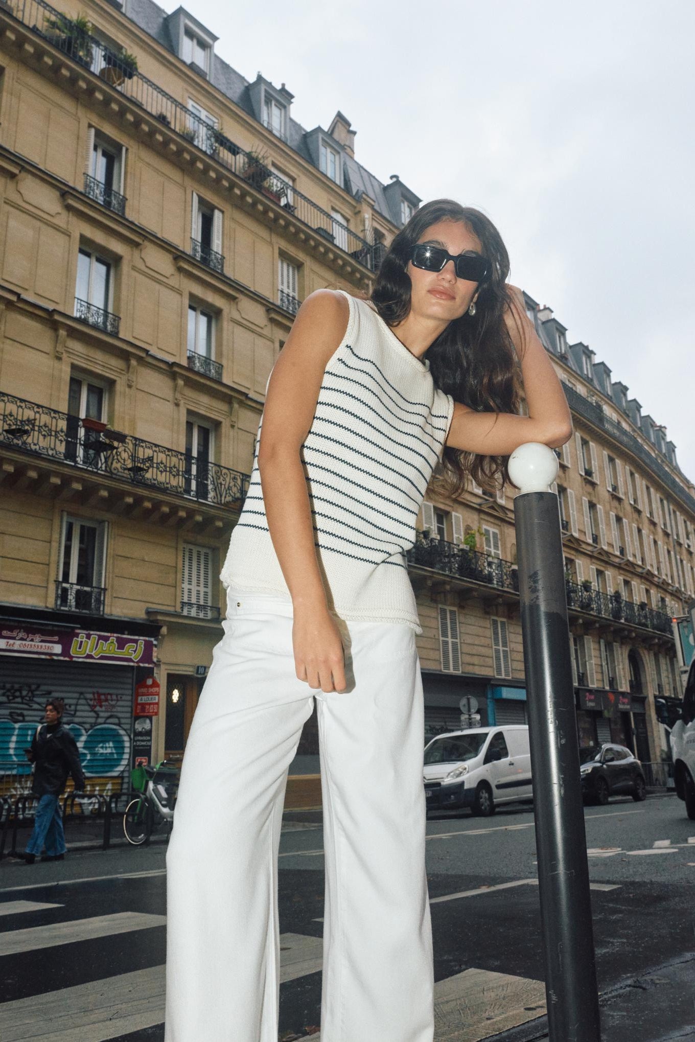 Woman in striped top and white pants standing on a city street with buildings in the background