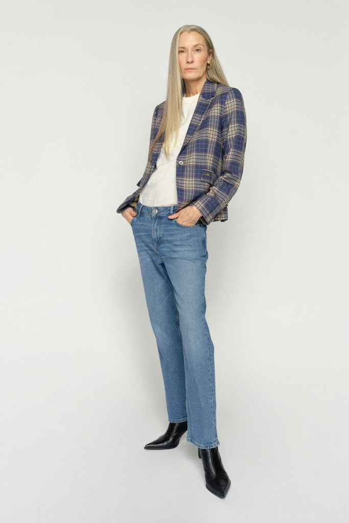 Woman wearing a plaid blazer, white shirt, and blue jeans against a grey background