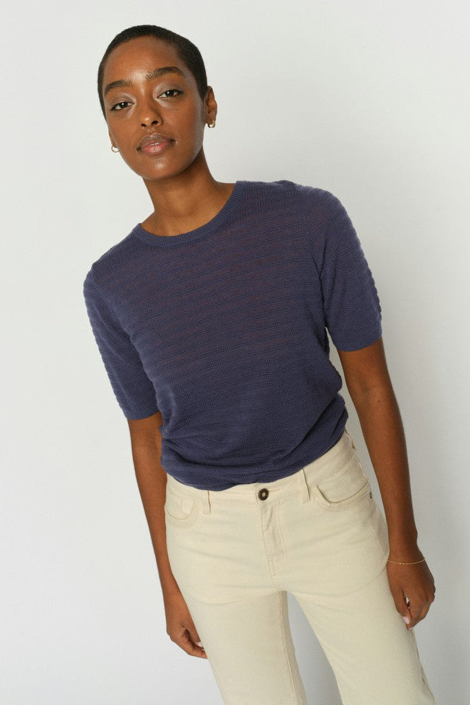 Model wearing a blue short sleeve textured sweater with round neck and cream jeans on a white background