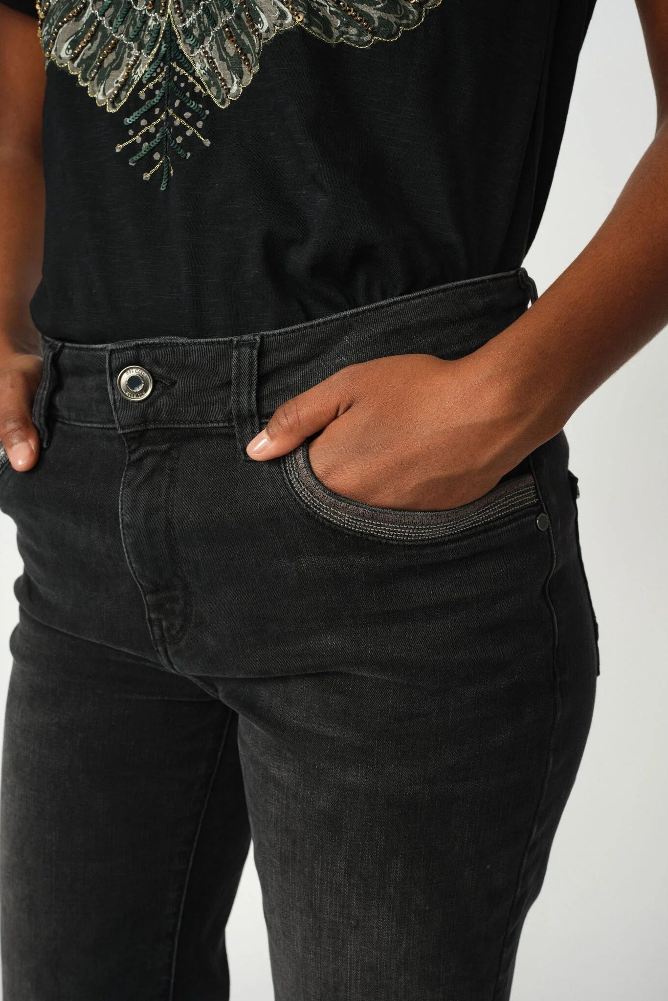 Person wearing black jeans and a black shirt with a textured collar on a light gray background