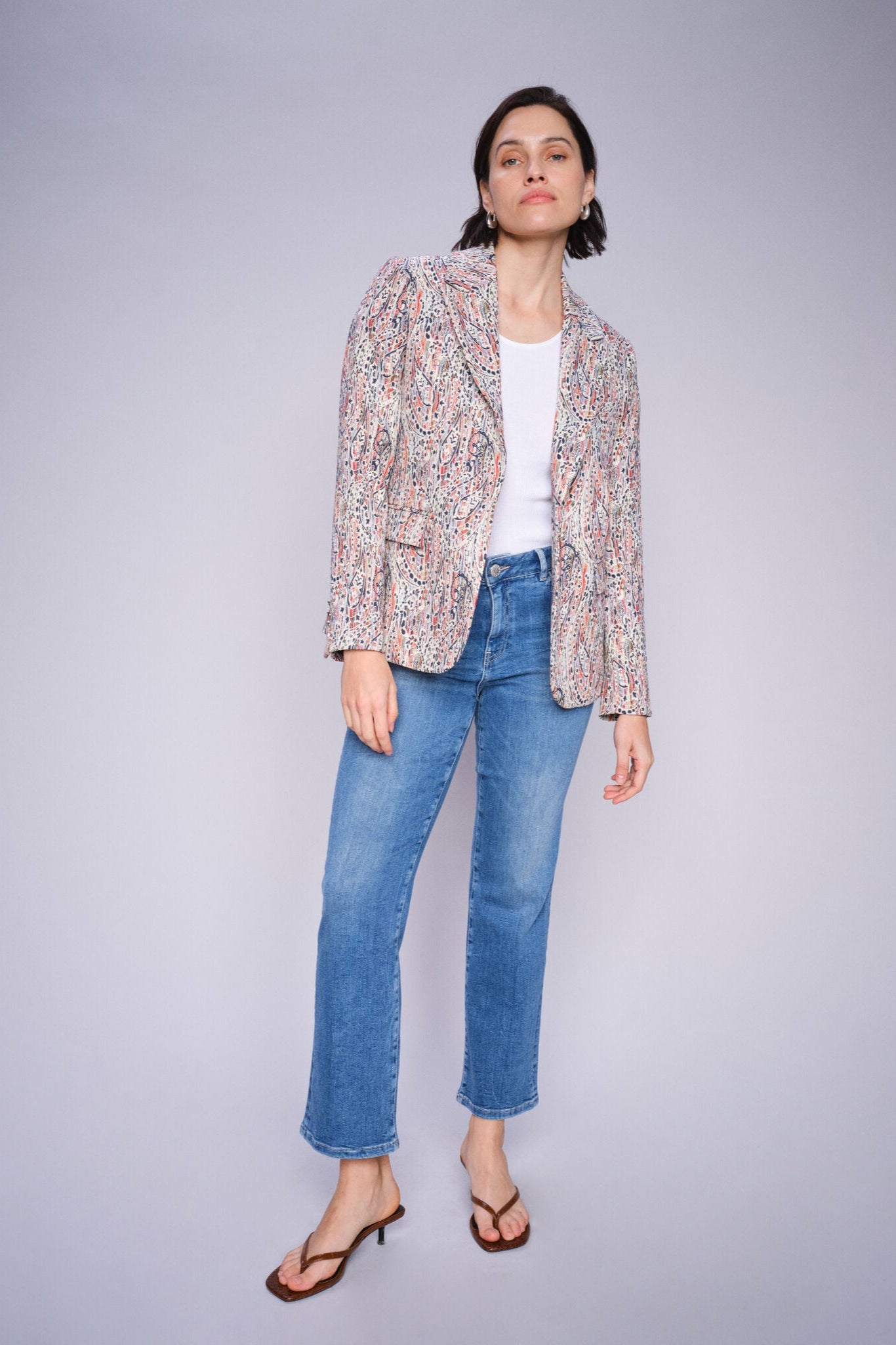 Woman posing in a floral jacket and Mid Blue slightly flared cropped blue jeans on a gray background