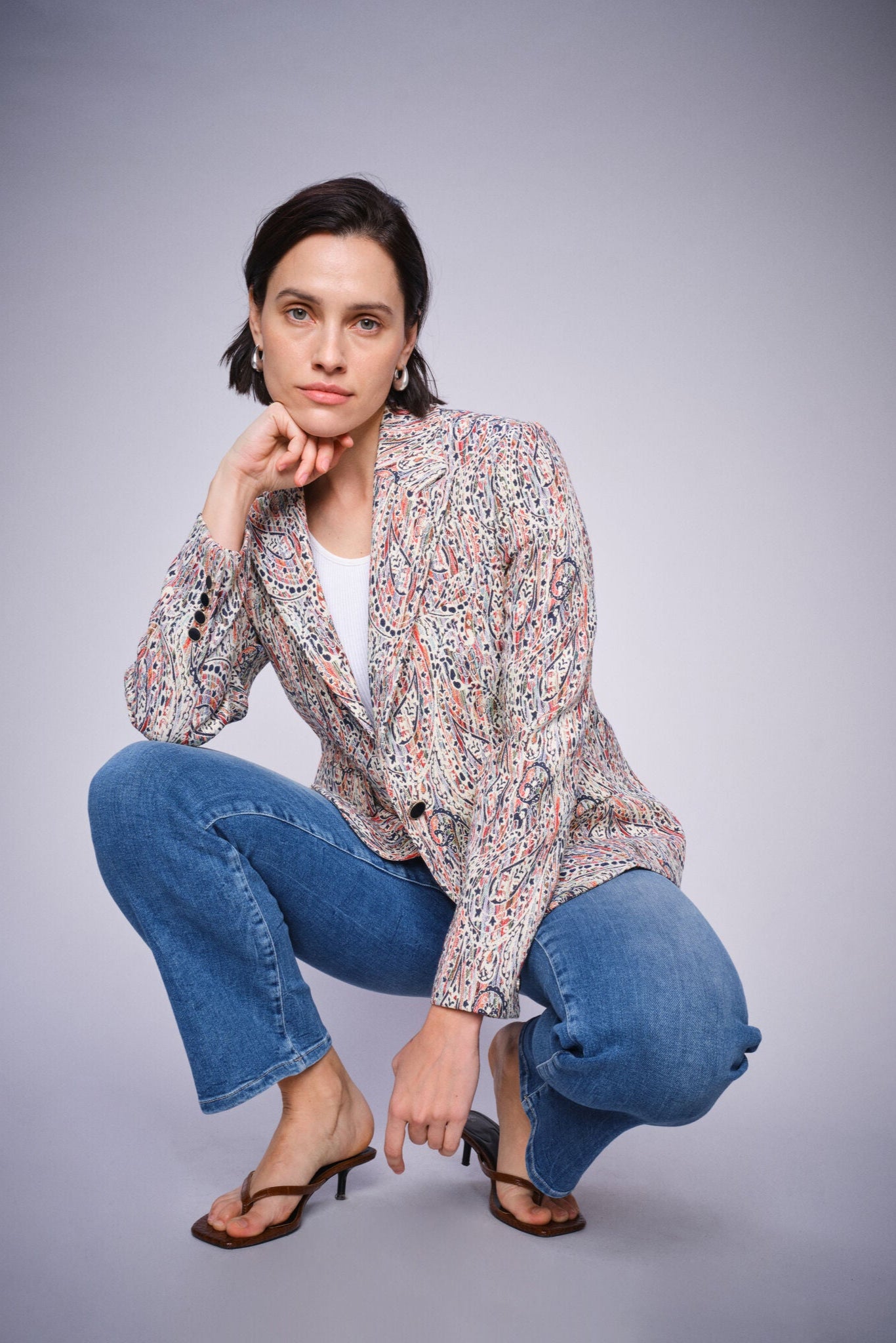Woman posing in a floral jacket and Mid Blue slightly flared cropped blue jeans on a gray background