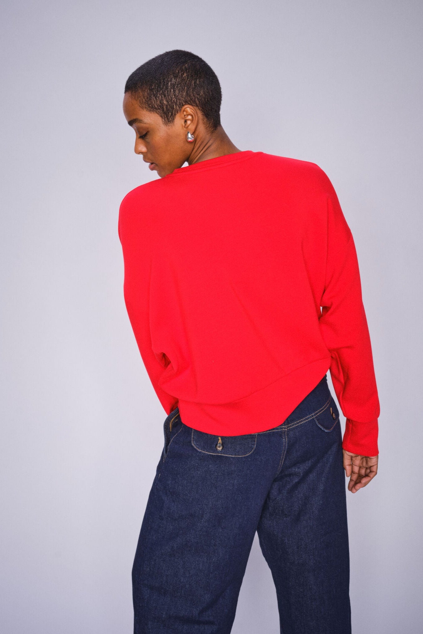 Model wearing a red sweater and blue jeans on a plain background