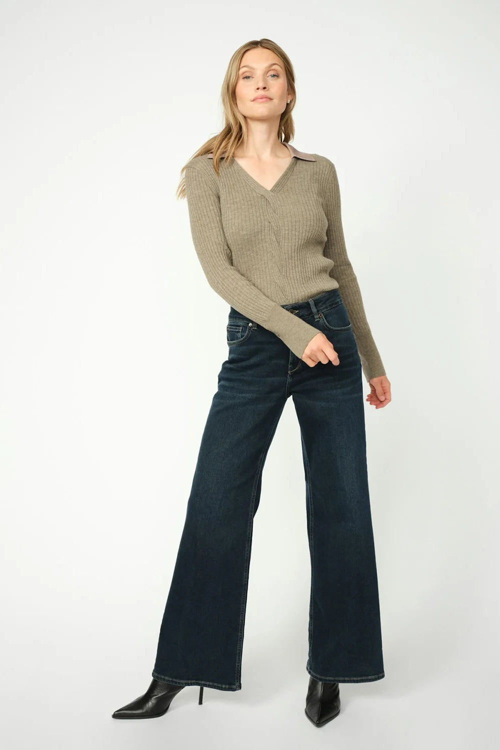 Women wearing dark blue wide leg jeans and a neutral sweater and black boots on a white background. 