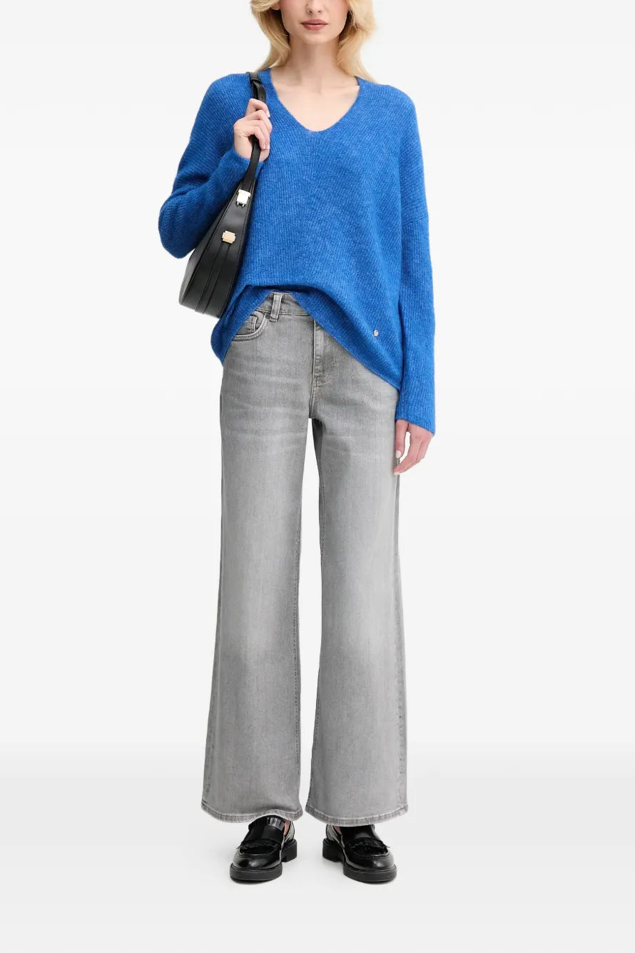 Person wearing a blue sweater and gray jeans on a white background