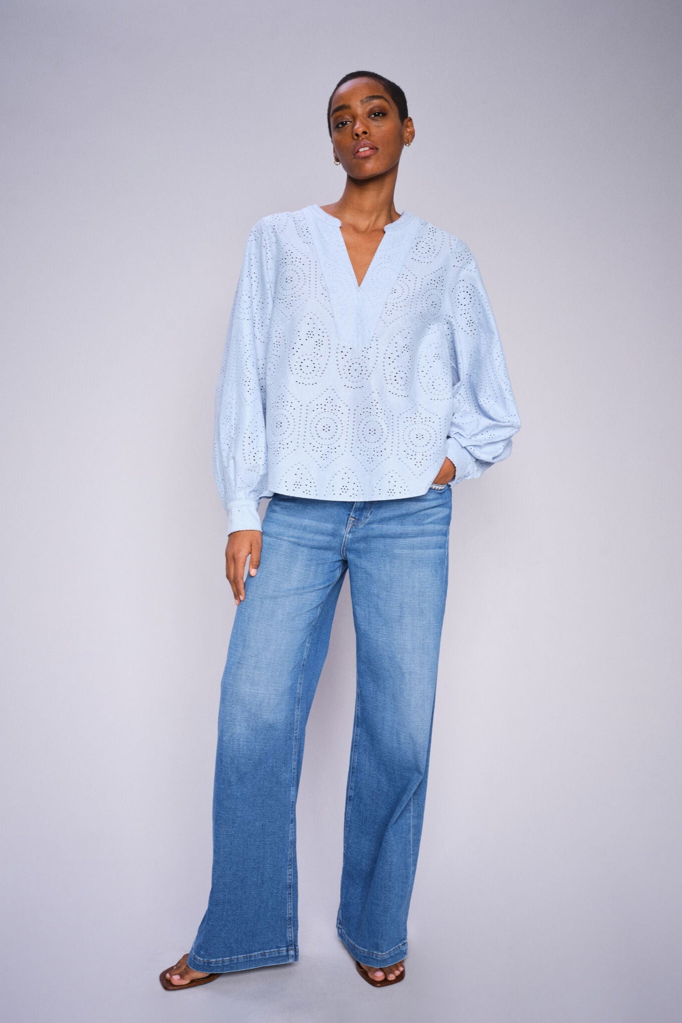 Model wearing a light blue shirt and wide leg light blue jeans on a white background