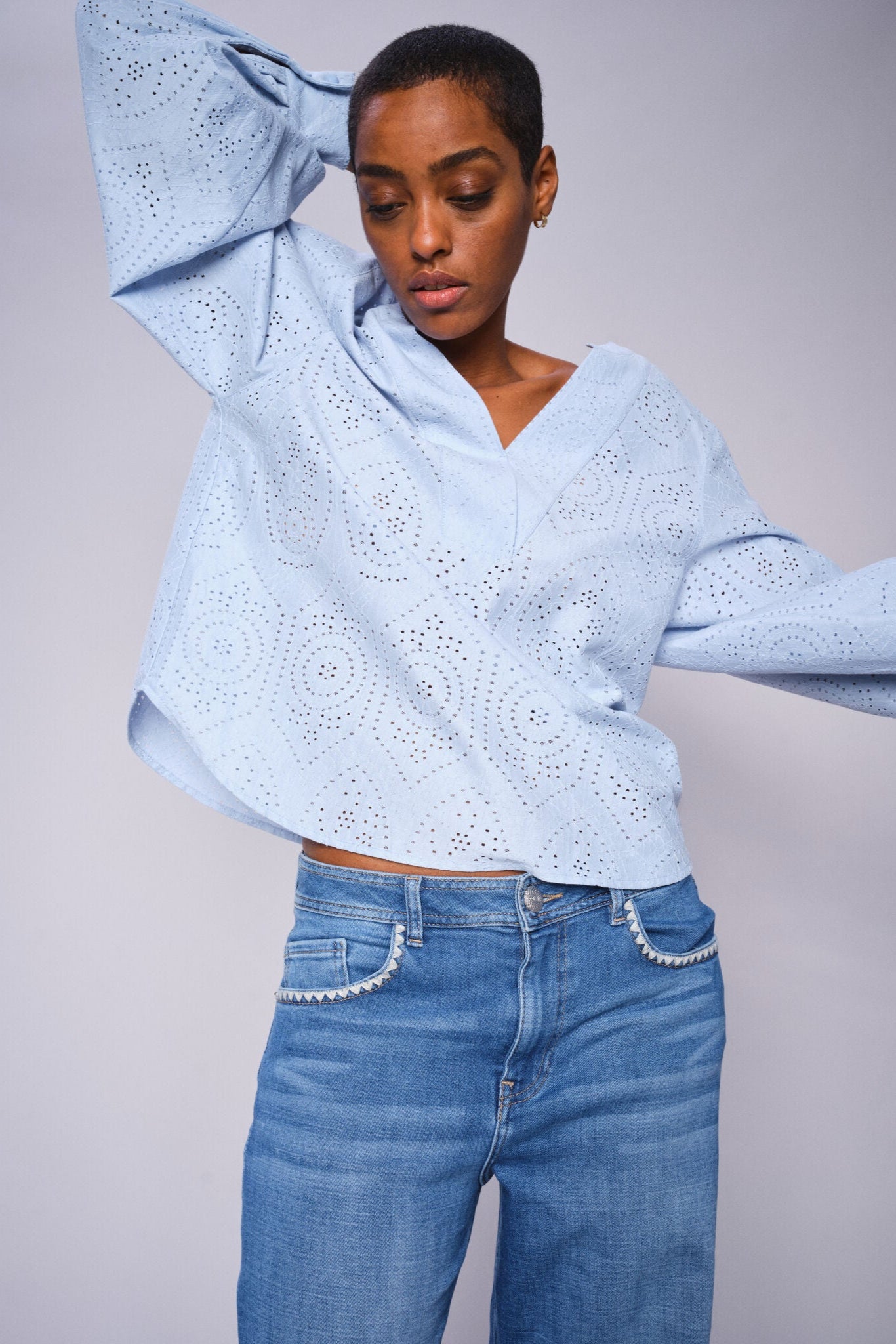 Model wearing a light blue shirt and wide leg light blue jeans on a white background