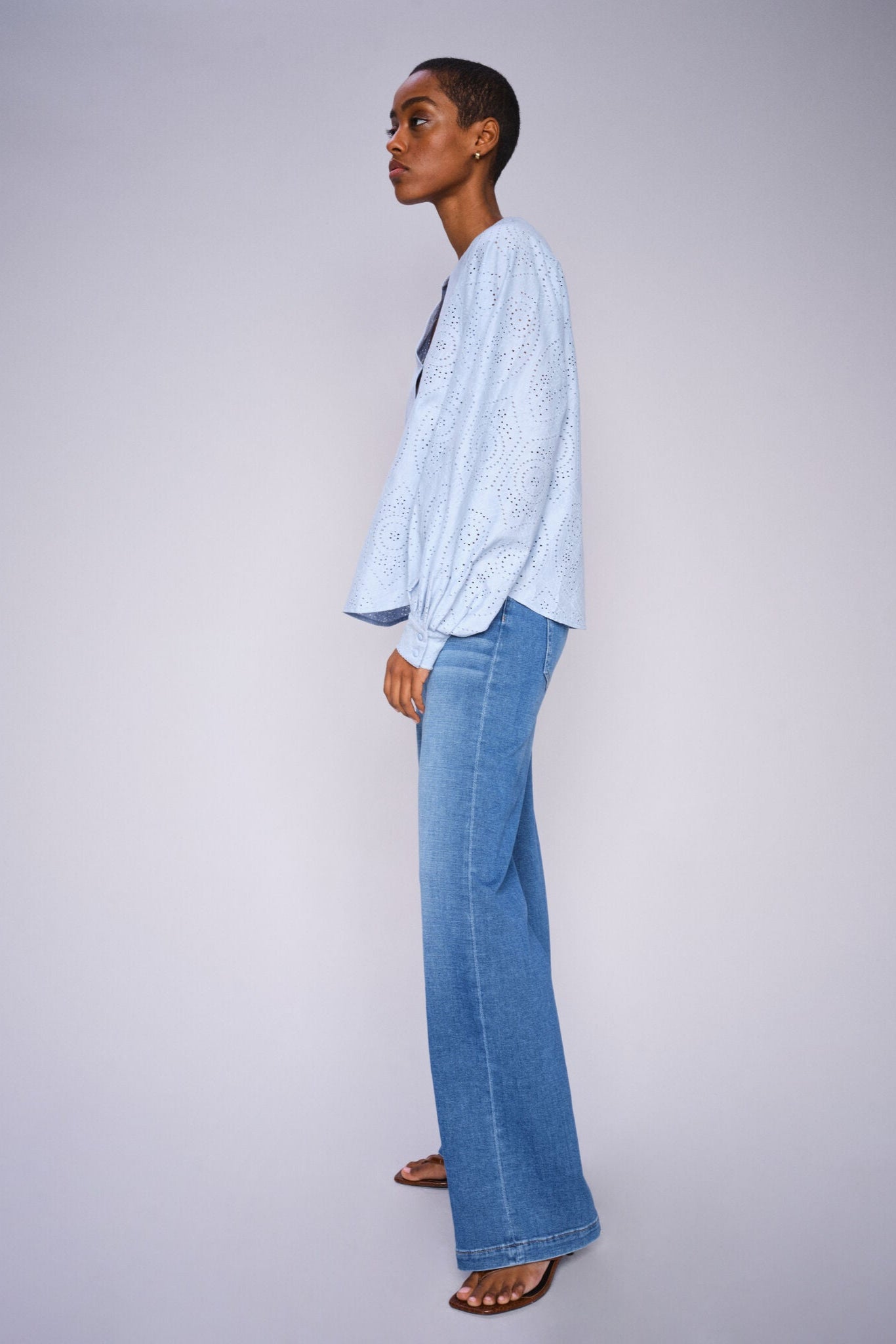Model wearing a light blue shirt and wide leg light blue jeans on a white background