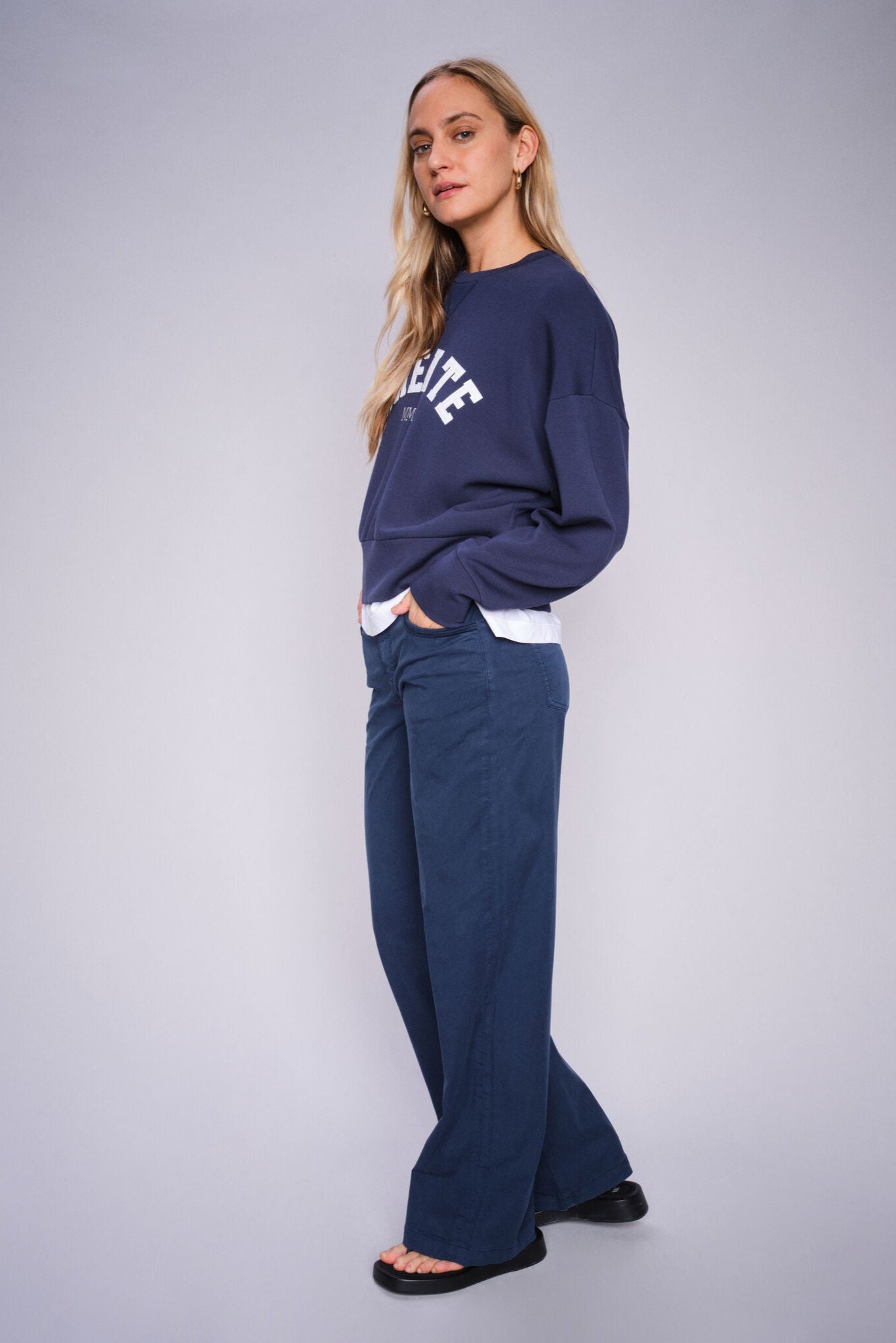 Woman wearing a navy blue sweatshirt and blue wide leg pants on a gray background