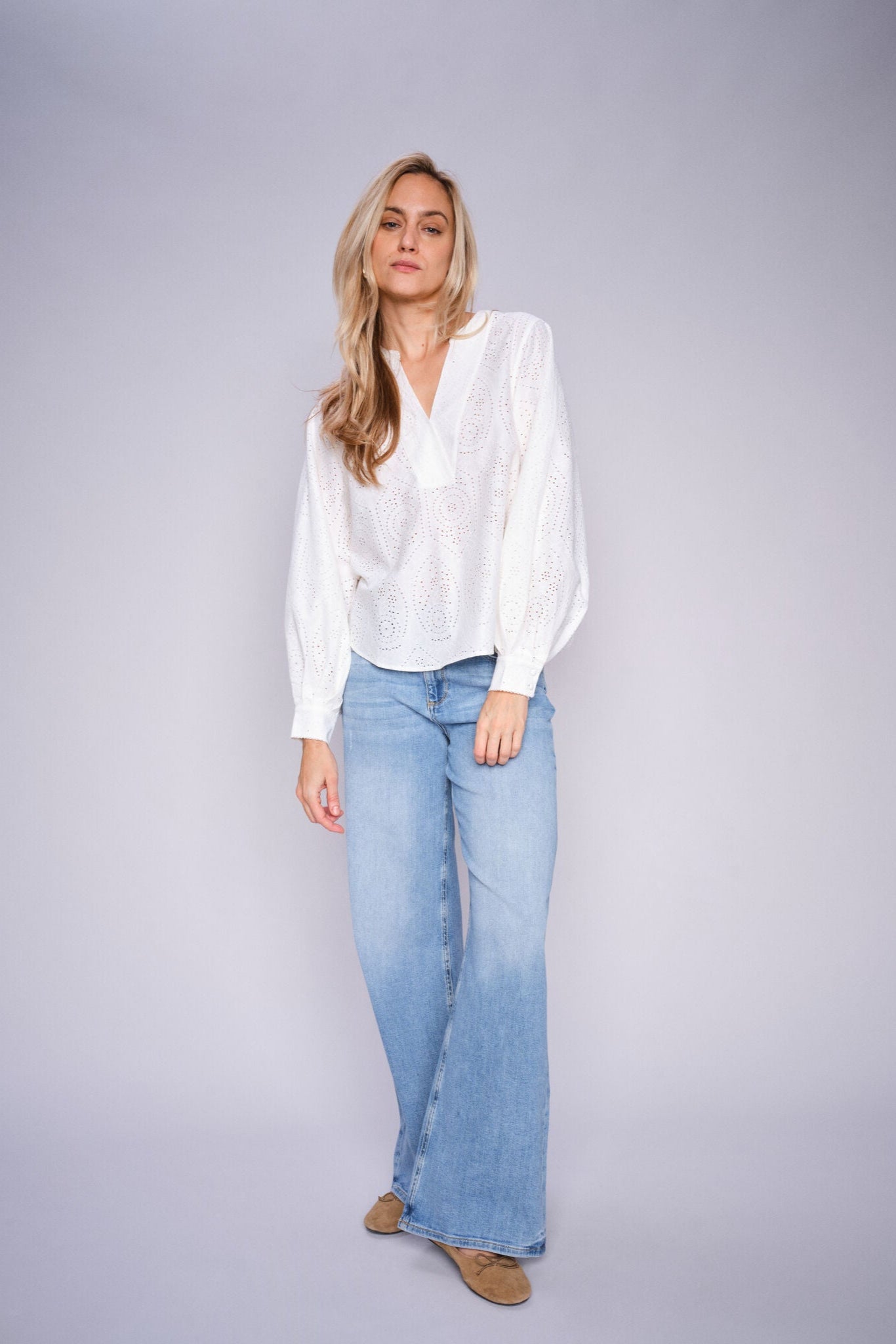 Woman wearing a white blouse and light blue wide leg jeans on a gray background