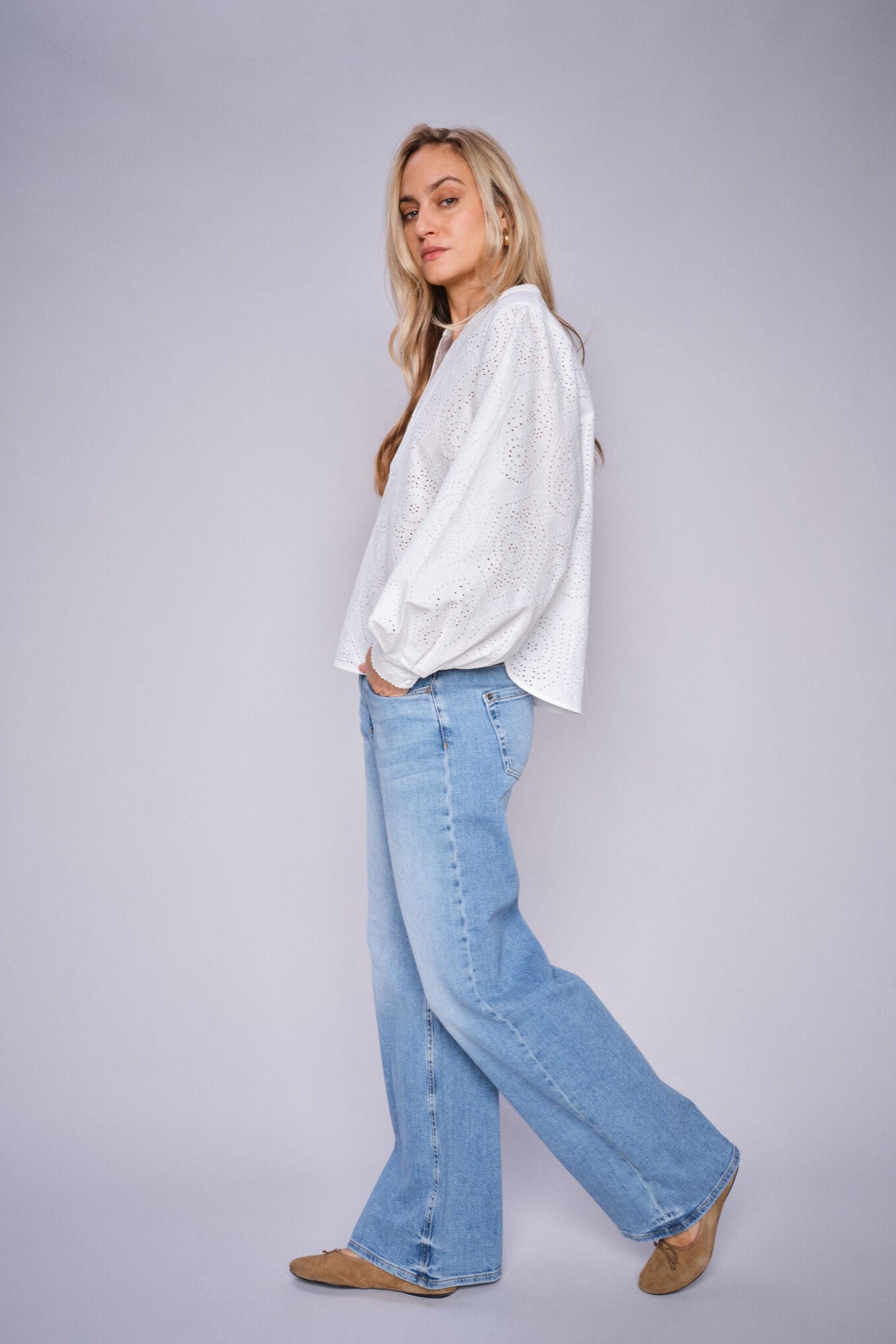 Woman wearing a white blouse and light blue wide leg jeans on a plain background