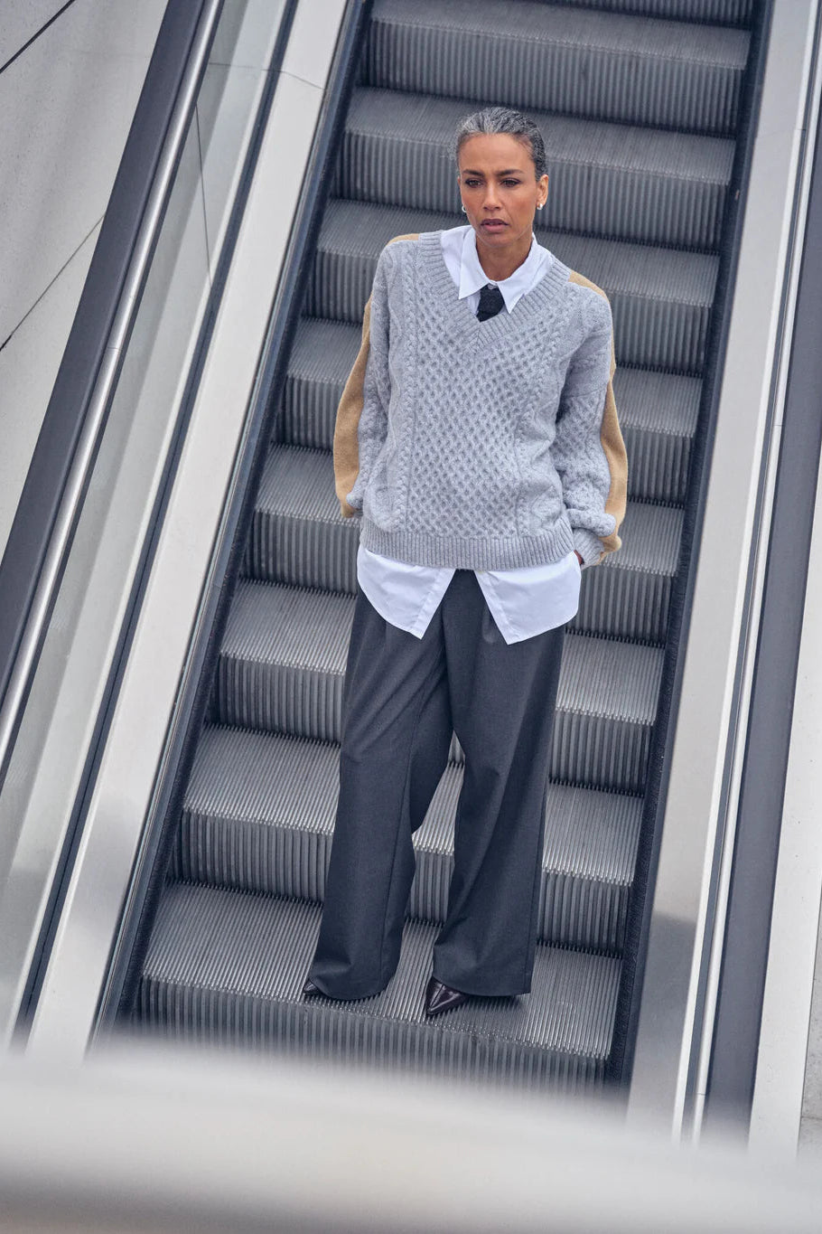 Person wearing a gray sweater and dark pants on an escalator