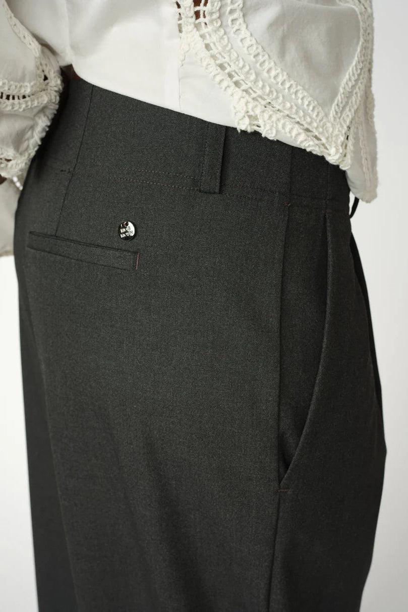 Dark gray pleated pants with a white lace top on a light gray background