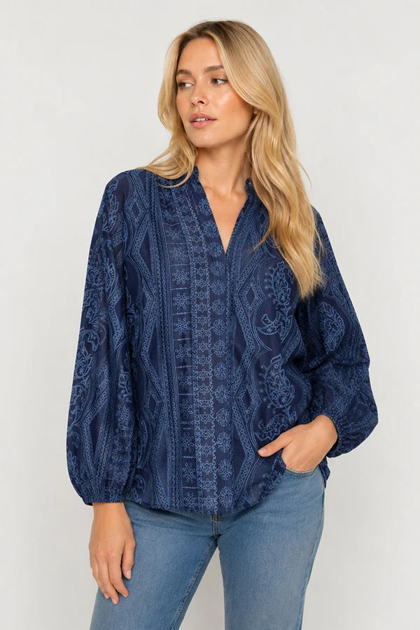 A model wearing a  long-sleeve blouse in navy blue with a light blue paisley and geometric pattern and light blue jeans on a plain background. 