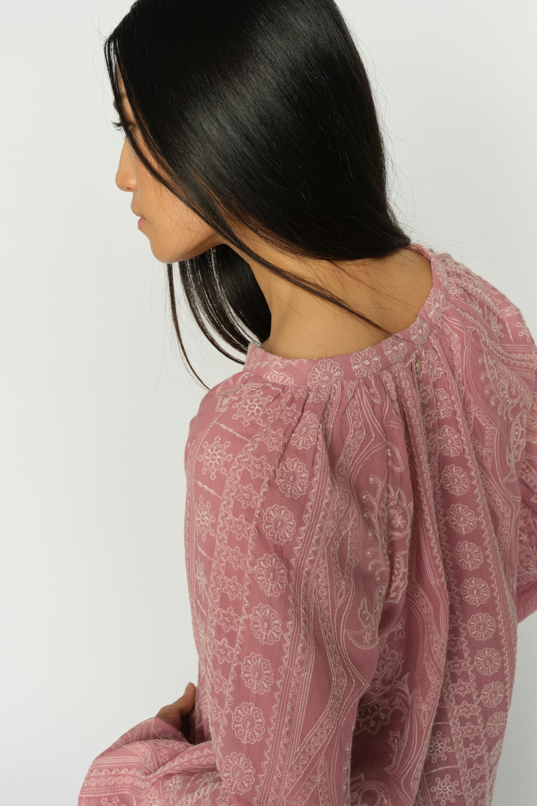 Women shown from back wearing a pink long-sleeve blouse with a white paisley and geometric pattern, featuring a split V-neckline and gathered cuffs, shown against a plain white background.