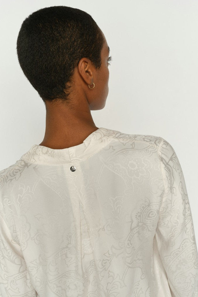 Woman shown from the back wearing an off-white long-sleeve blouse with delicate floral embroidery, shown from the back against a plain white background.