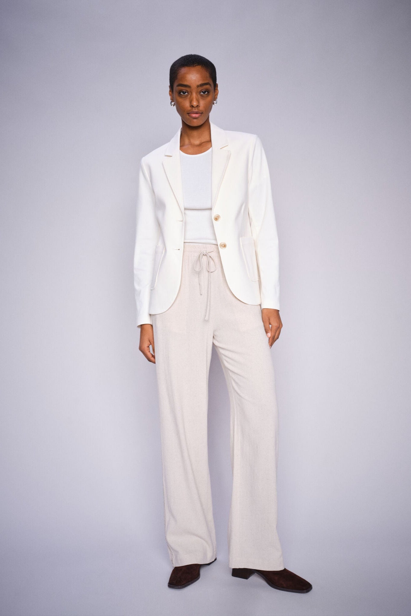 Model wearing beige straight leg pants with elastic waist band and draw string and a white blazer and brown boots on a white background