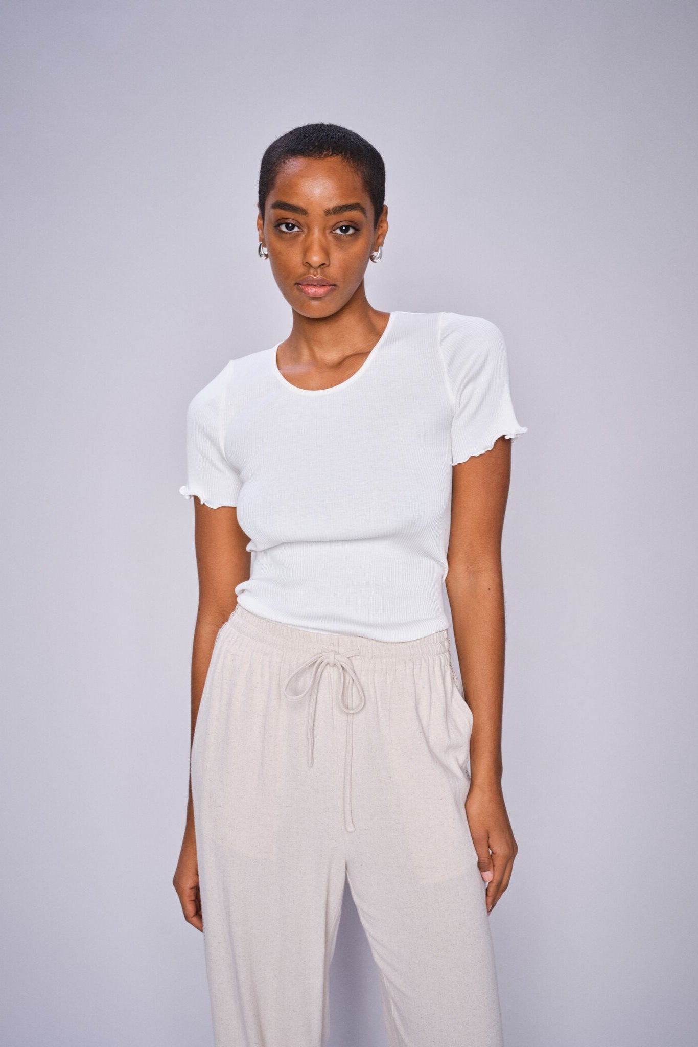 Model wearing white t shirt and beige pants with draw string waist on a white background. 