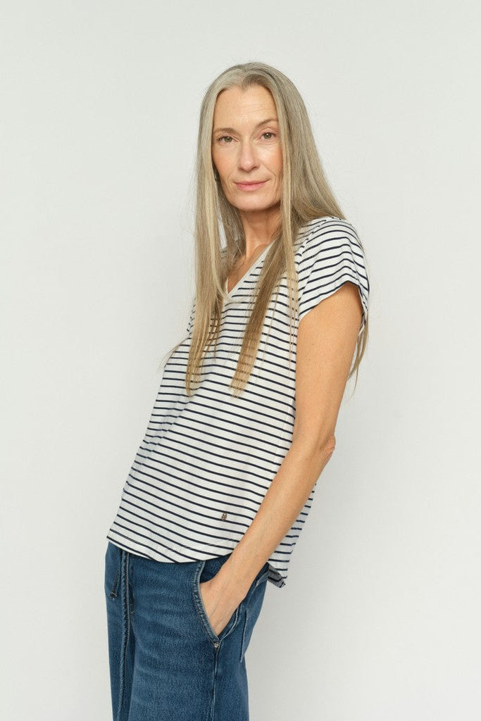 Woman wearing a v neck blue and white striped tee shirt and jeans against a plain background