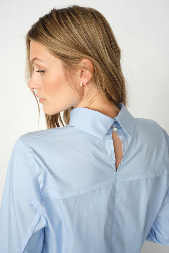 Woman wearing a light blue shirt with a cut-out design on the back on a white background
