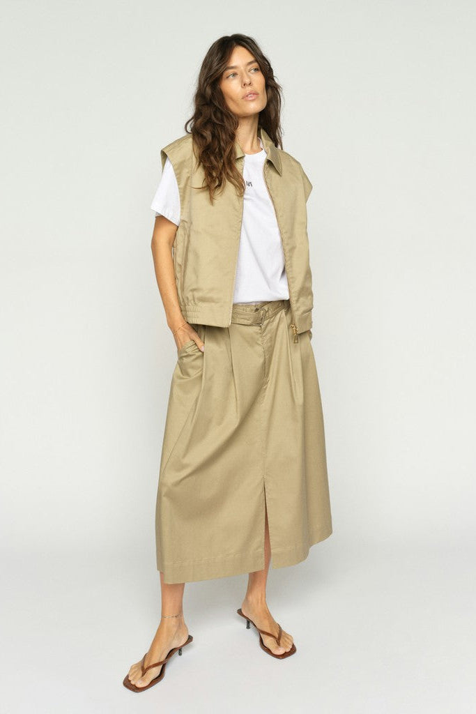 Woman wearing a beige waist coat  over a white tee shirt  with a matching beige midi skirt on a plain background