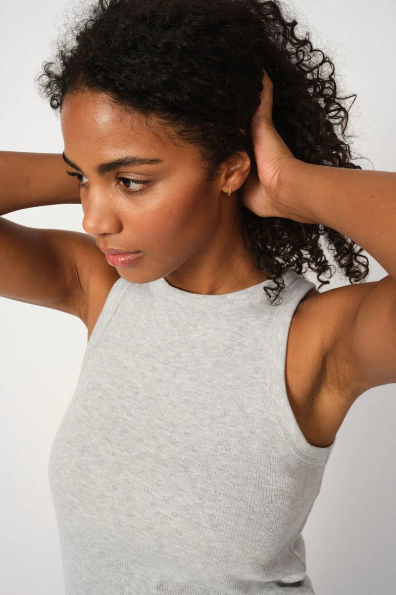 Woman in a gray tank top with her hands behind her head against a white background