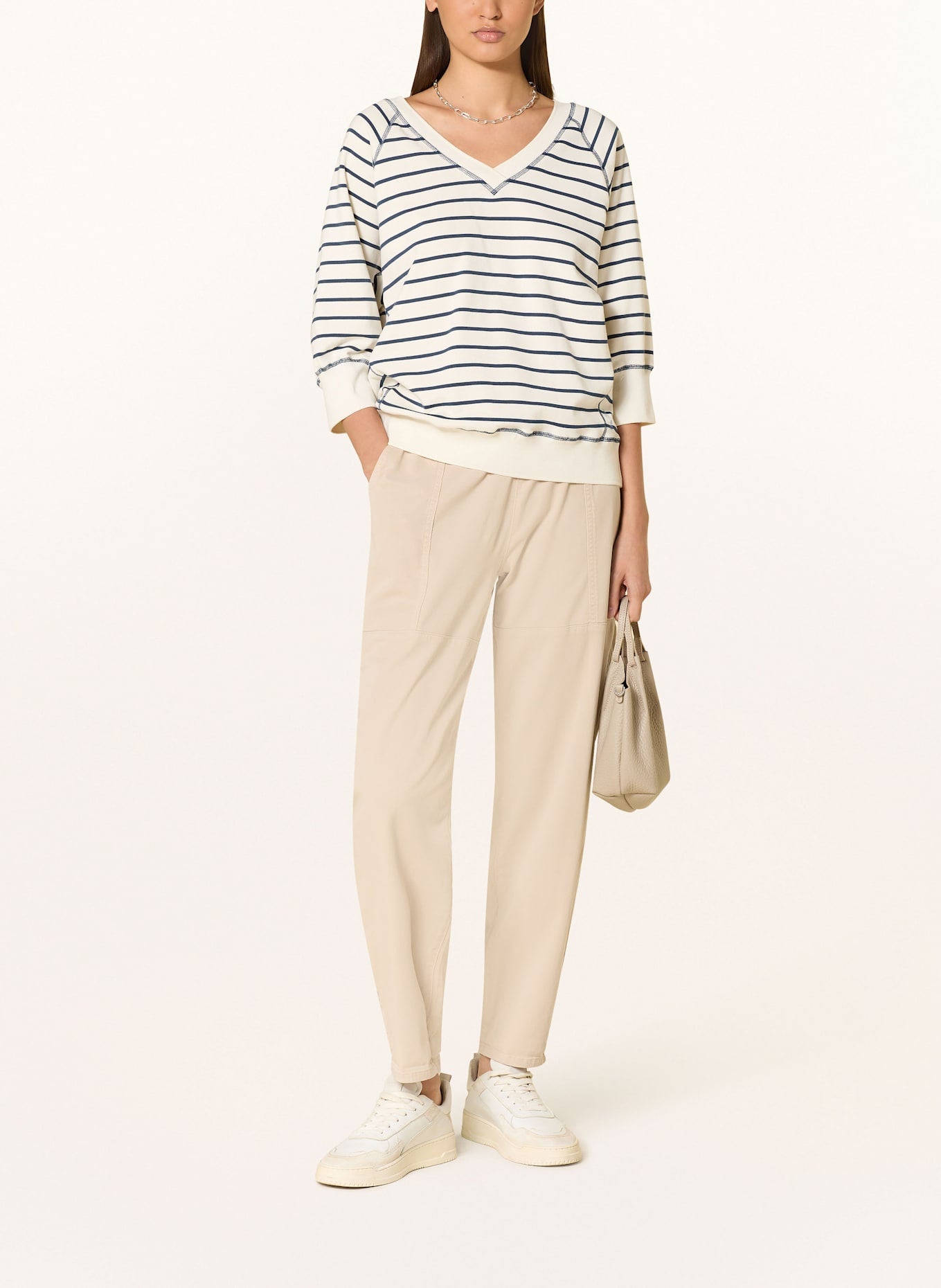 Model wearing Striped 3/4 sleeve sweatshirt with black and white stripes paired with cream pants and white sneakers. 